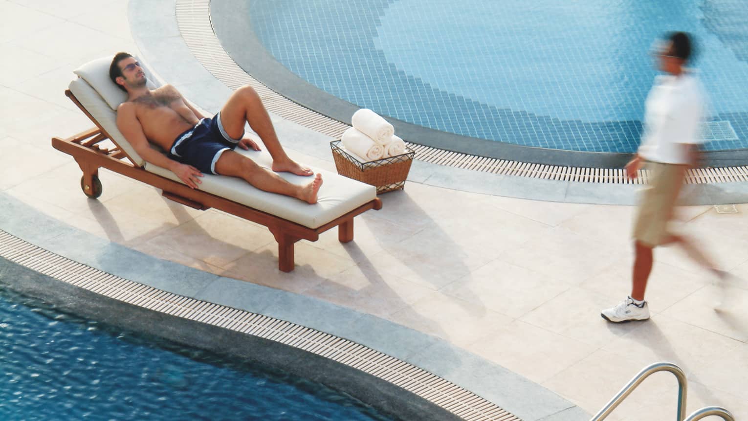 Man in swimsuit relaxes on beach lounge chair by swimming pool