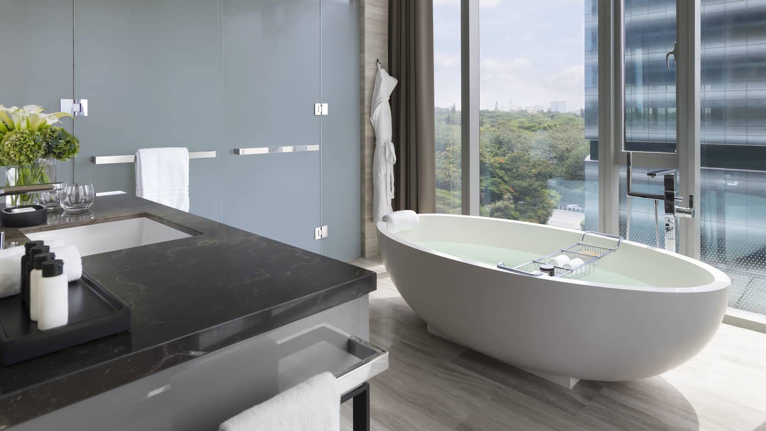 Bathroom with white free-standing tub set next to a floor-to-ceiling window