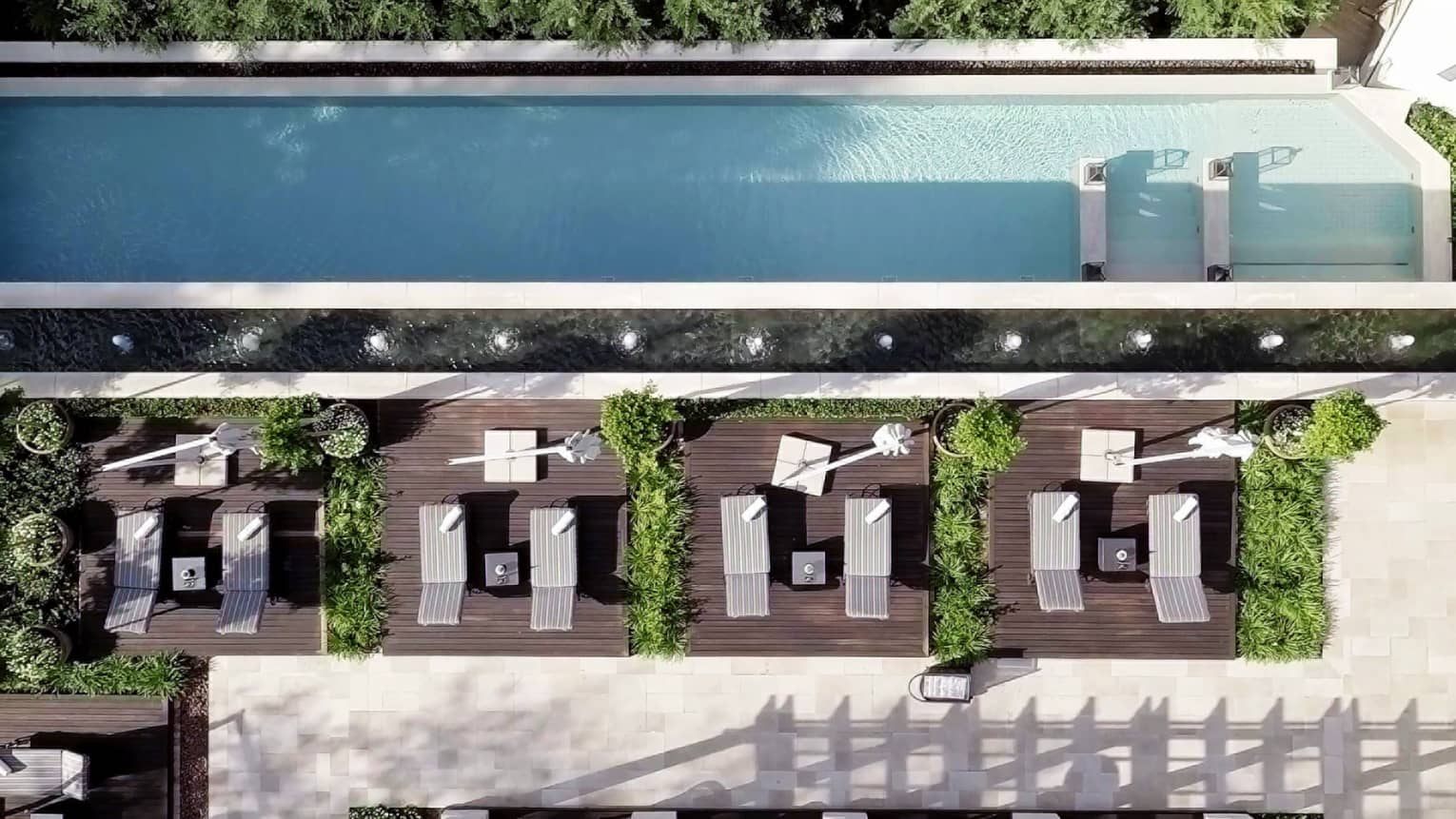 Aerial view of long rectangular outdoor swimming pool, lounge chairs on wood deck