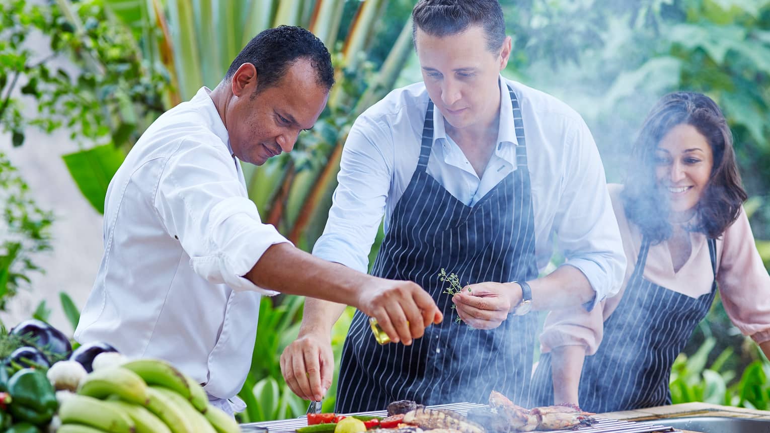 Chef, couple wearing aprons garnish meat, vegetables on outdoor grill