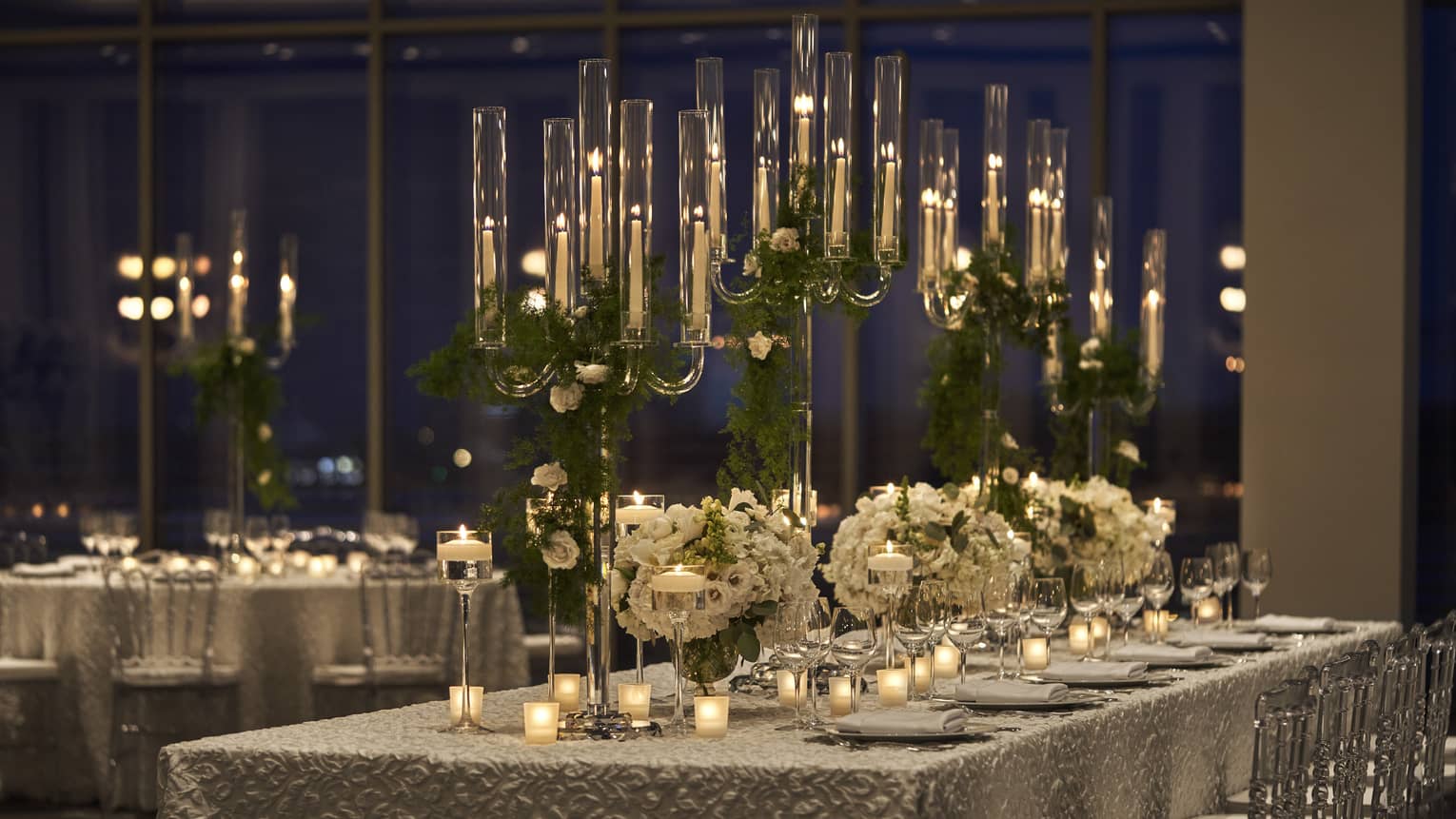 Long tables with table cloth, tall candles, and flowers.