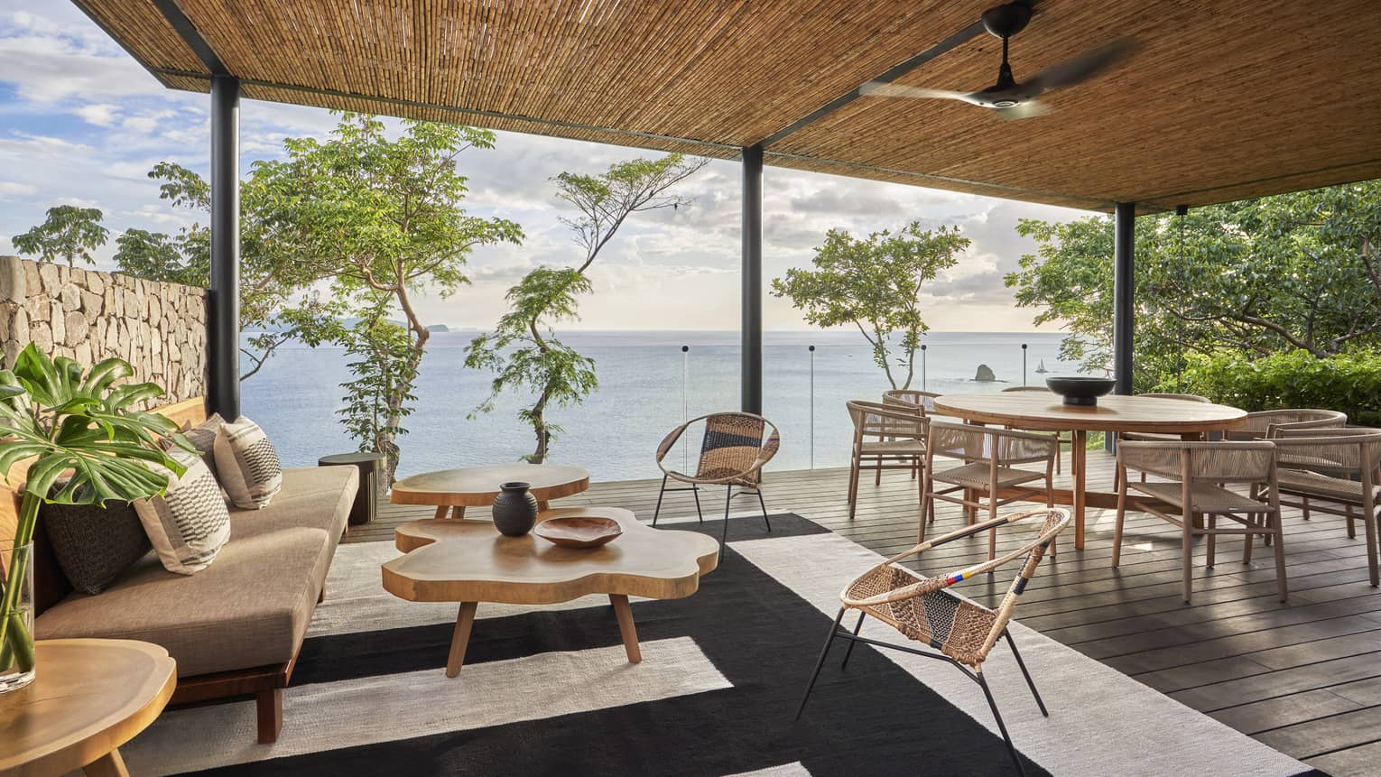 Covered outdoor wooden deck with dining table and contemporary lounge furniture overlooking the sea
