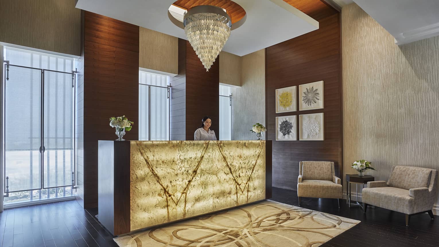 A yellow glass chandelier hangs over the welcome desk, adorned with soft yellow light and a brown rug. 