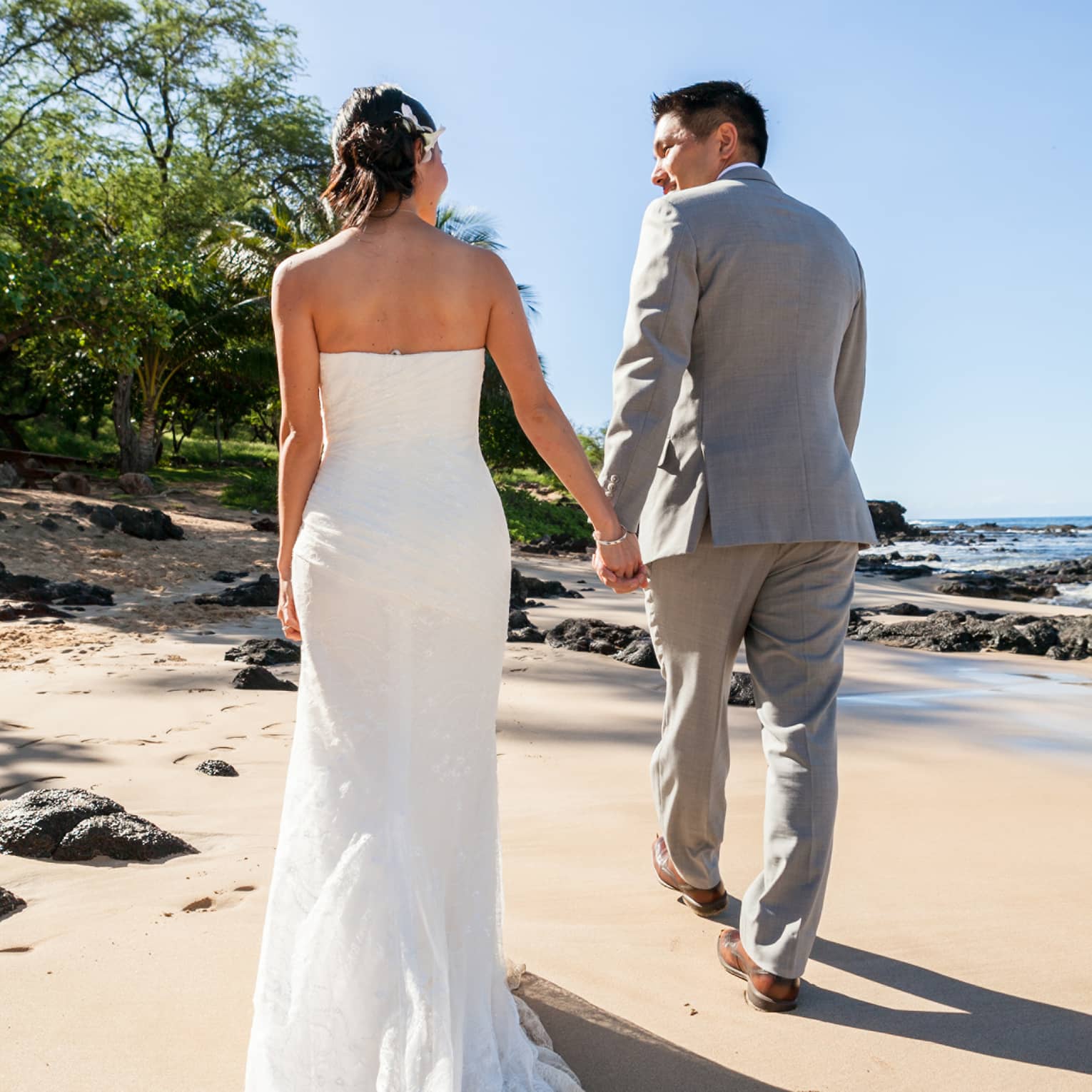Back of bride and groom as they walk along sand beach