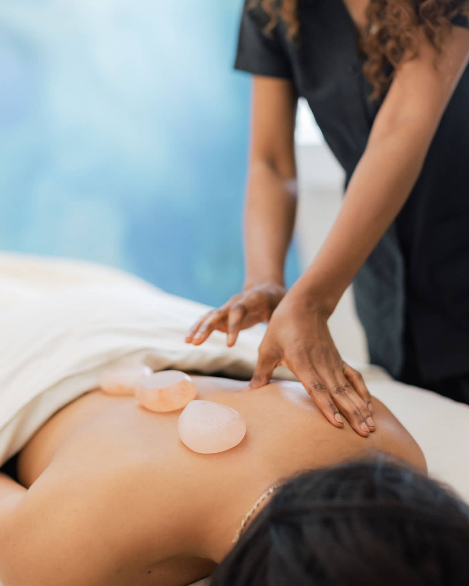 Masseuse places salt stones on a person's bare back