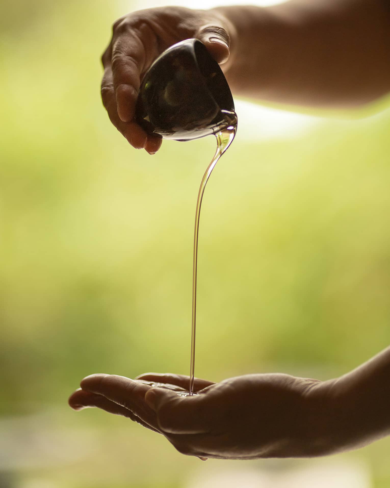 A set of hands pours massage oil from a ceramic bowl into a palm
