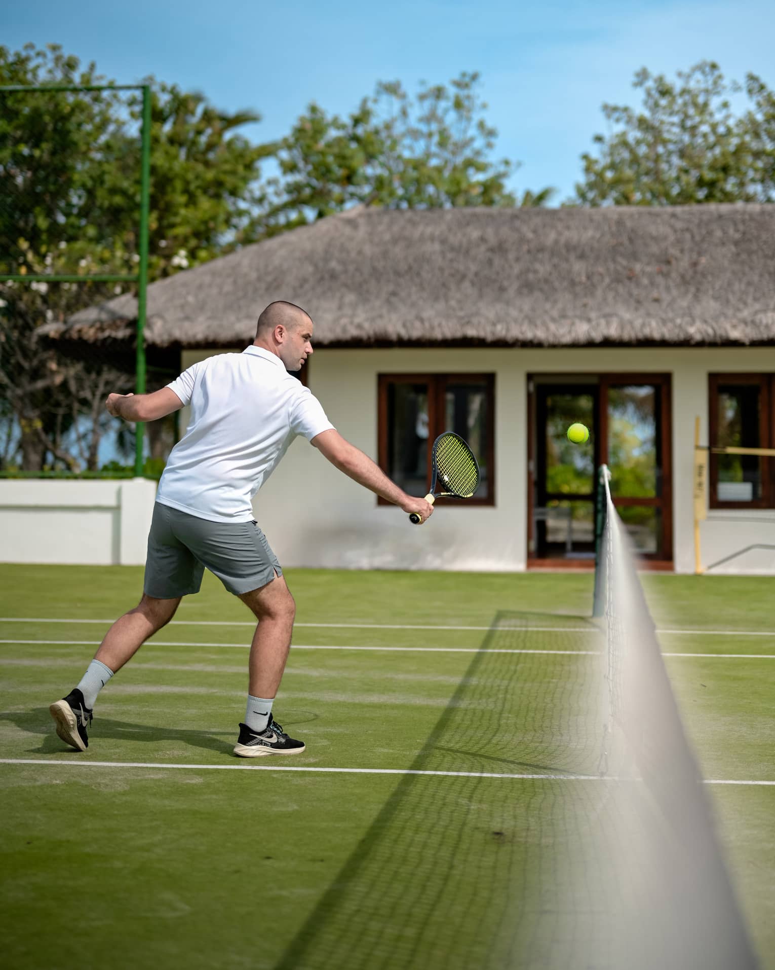 Person in white polo shirt and grey shorts practises tennis