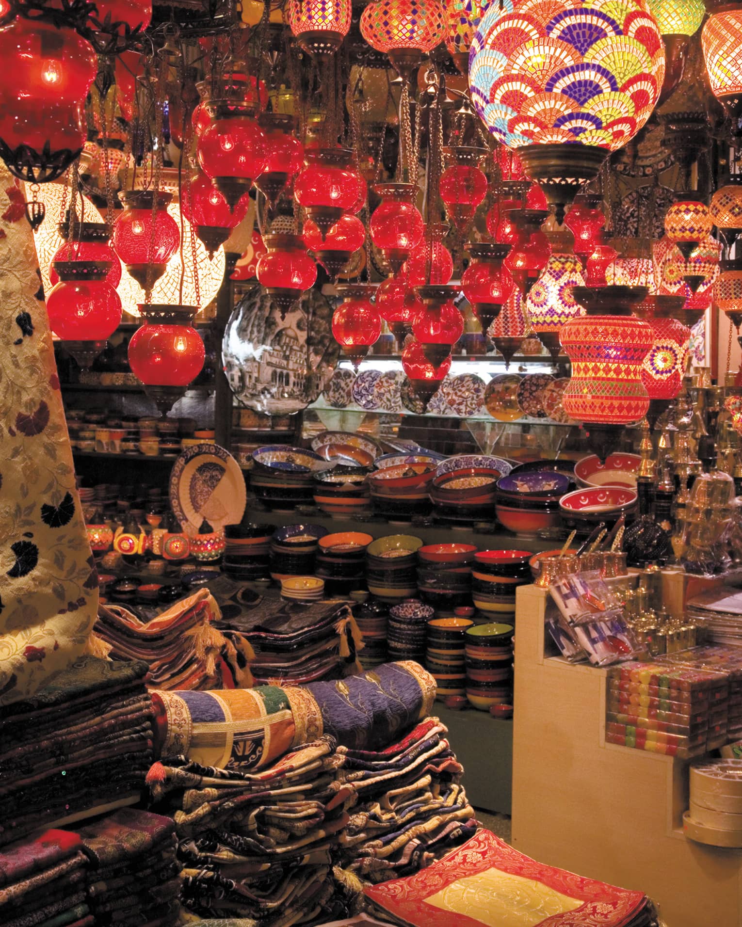 Red lanterns hang over shelves with decorative plates in Grand Bazaar