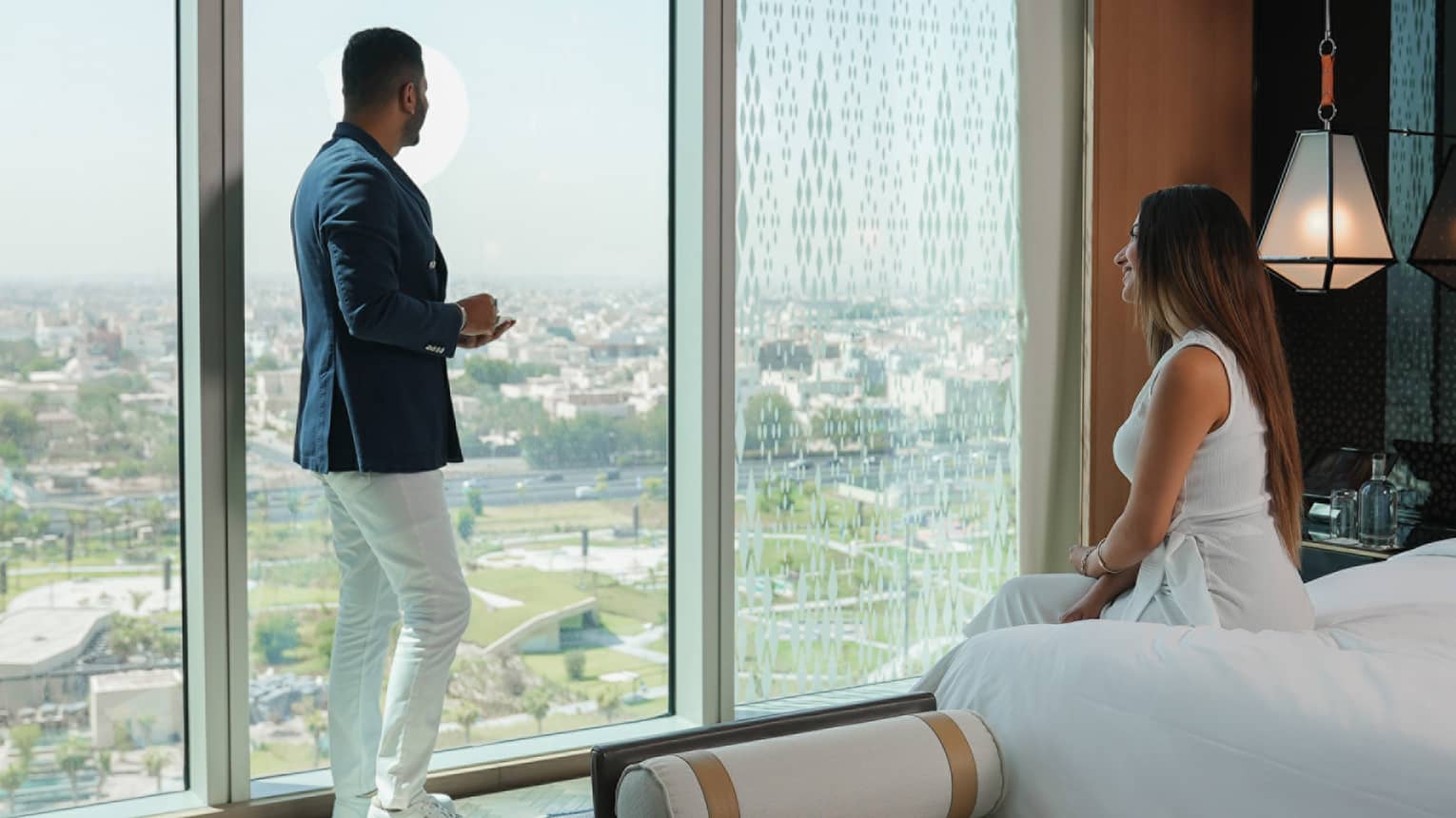 Man and woman in hotel room, looking out floor-to-ceiling window