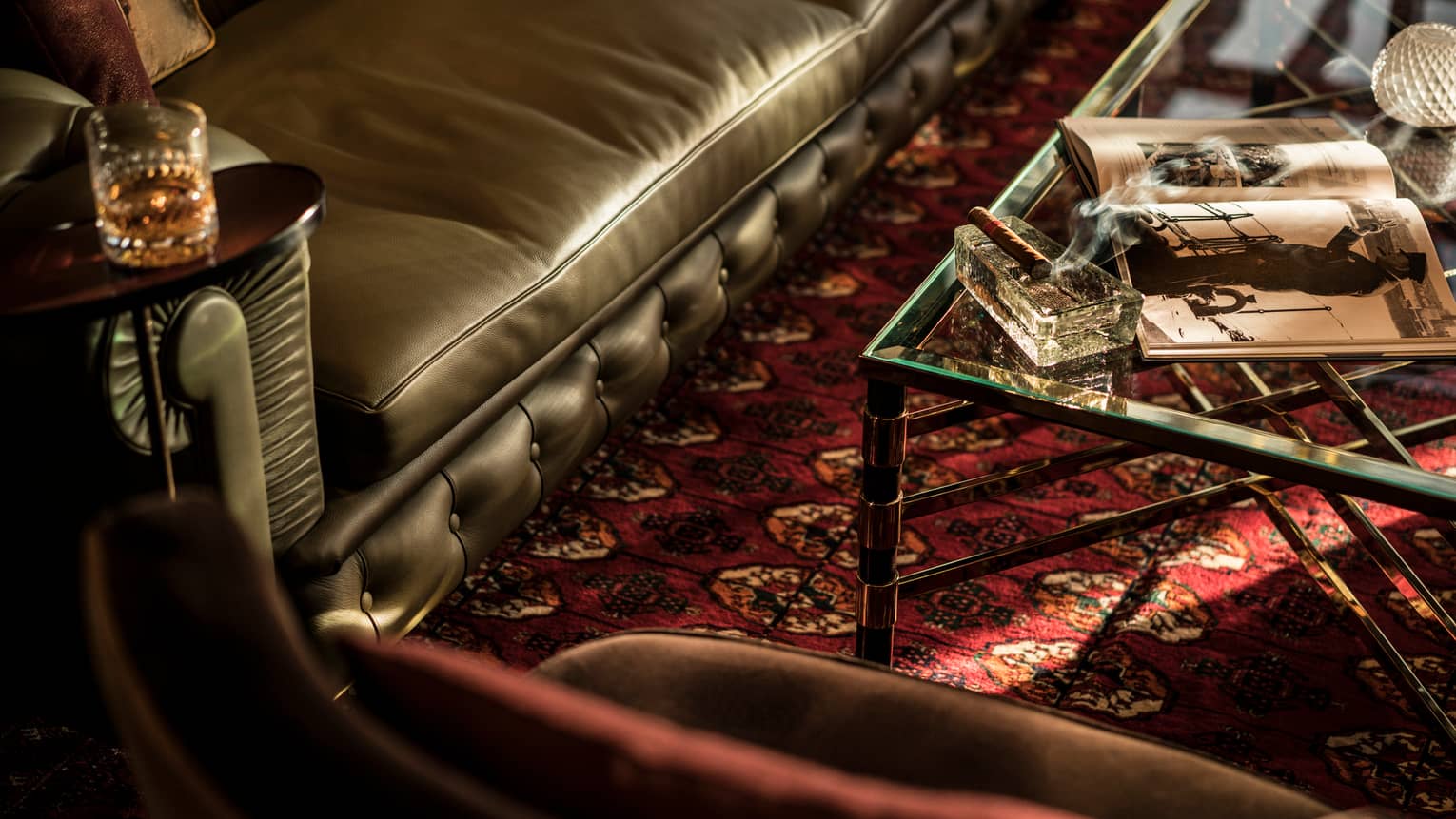 Close-up of corner of leather sofa with cocktail glass, cigar with smoke on tables