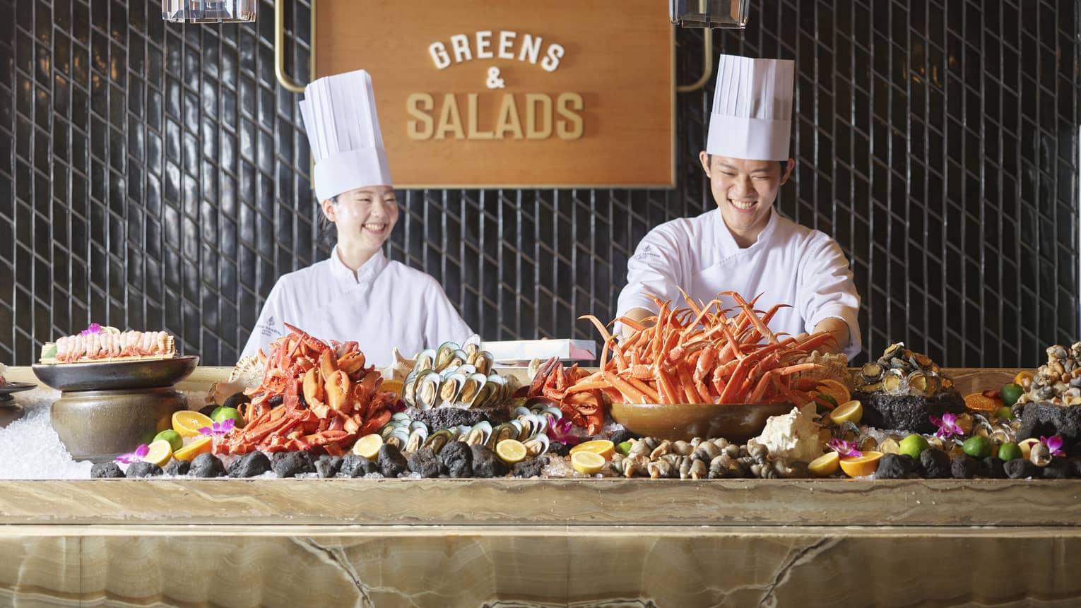 Two smiling chefs in tall white hats stand behind marbled counter with an assorted seafood display on ice