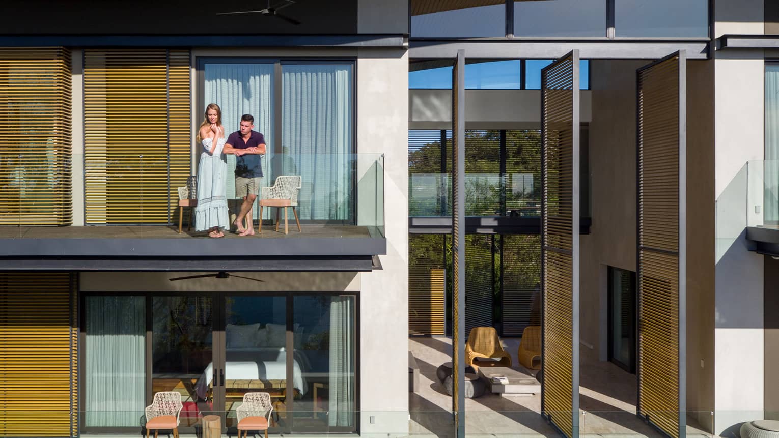 Man and woman stand on glass balcony of villa