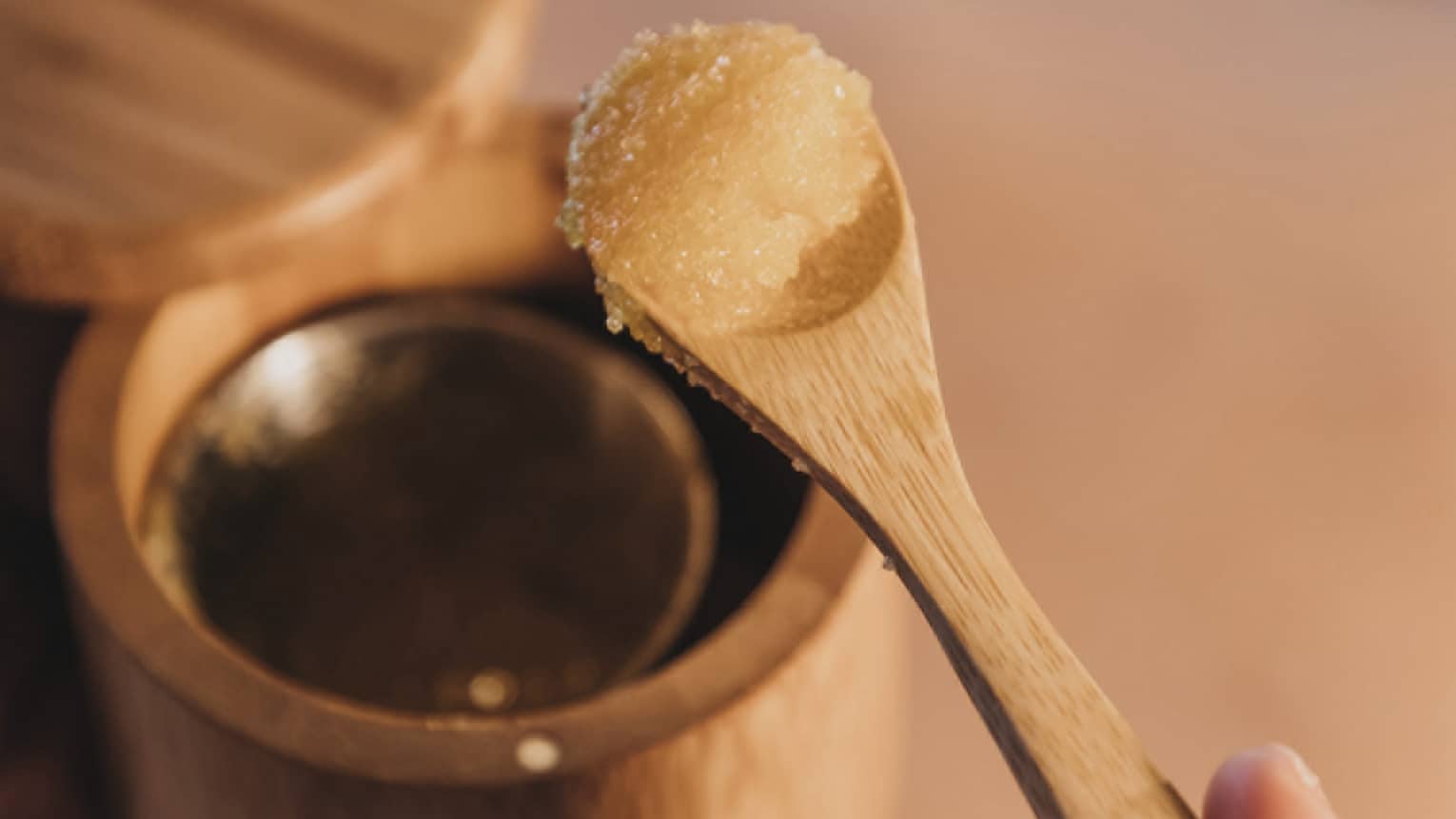 A spa member removing a spa treatment ingredient from a wooden cup with a spoon.