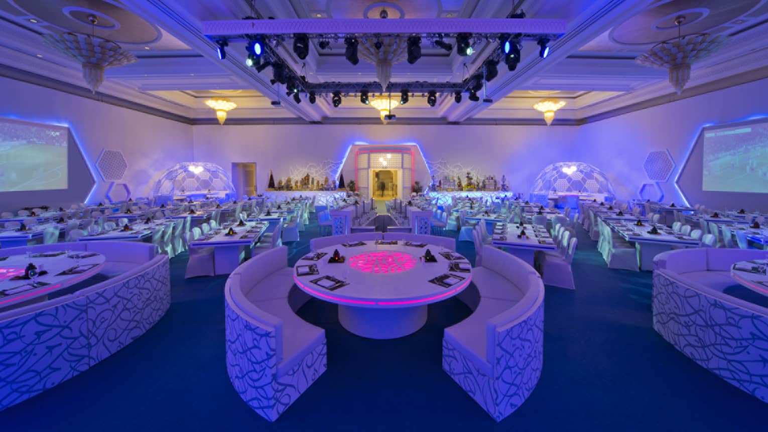 Modern wedding reception with curved white banquettes around tables with purple lights