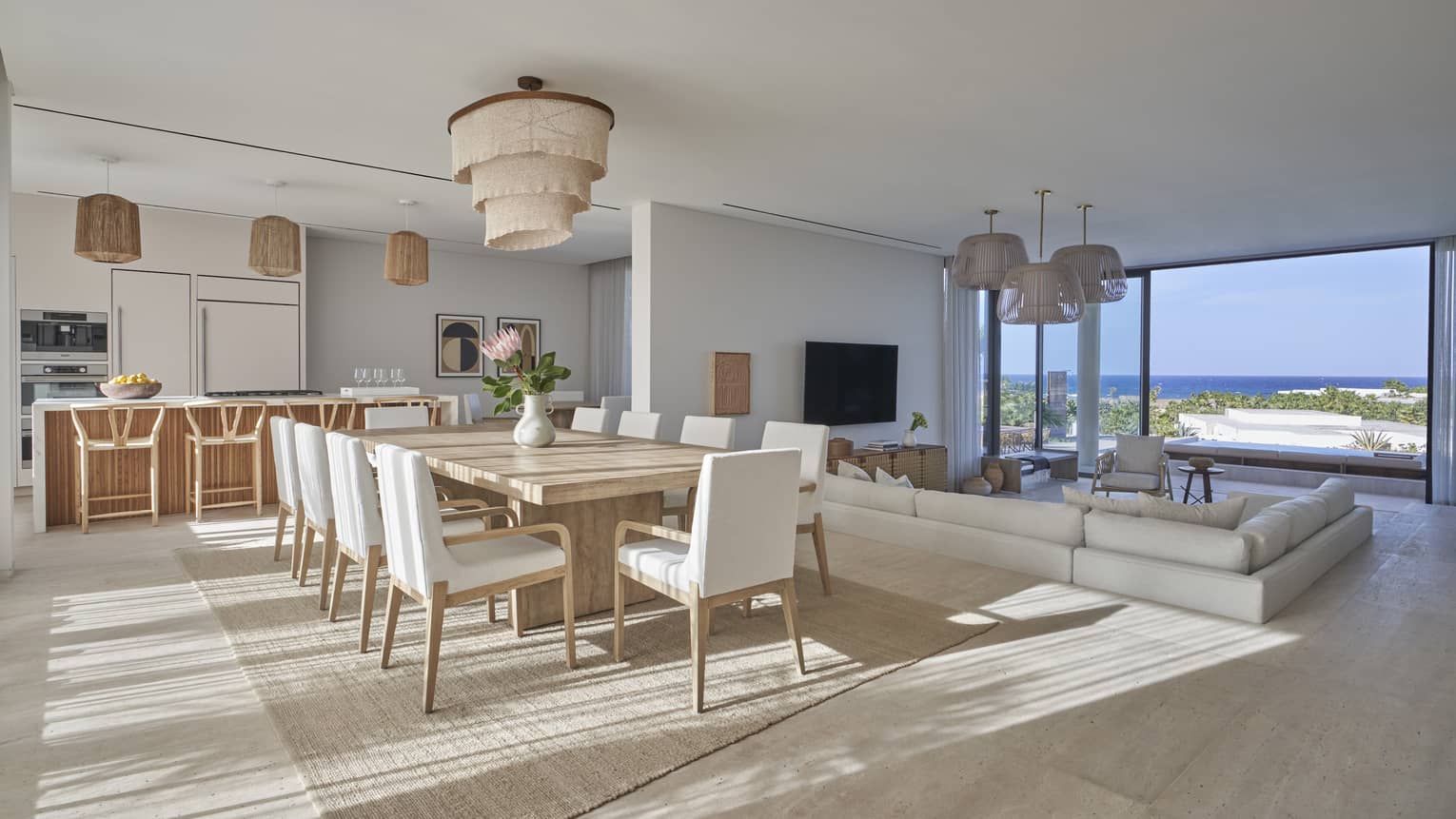 Modern open living area with dining table and white chairs, kitchen with barstools and sunken sectional facing tall windows and water view