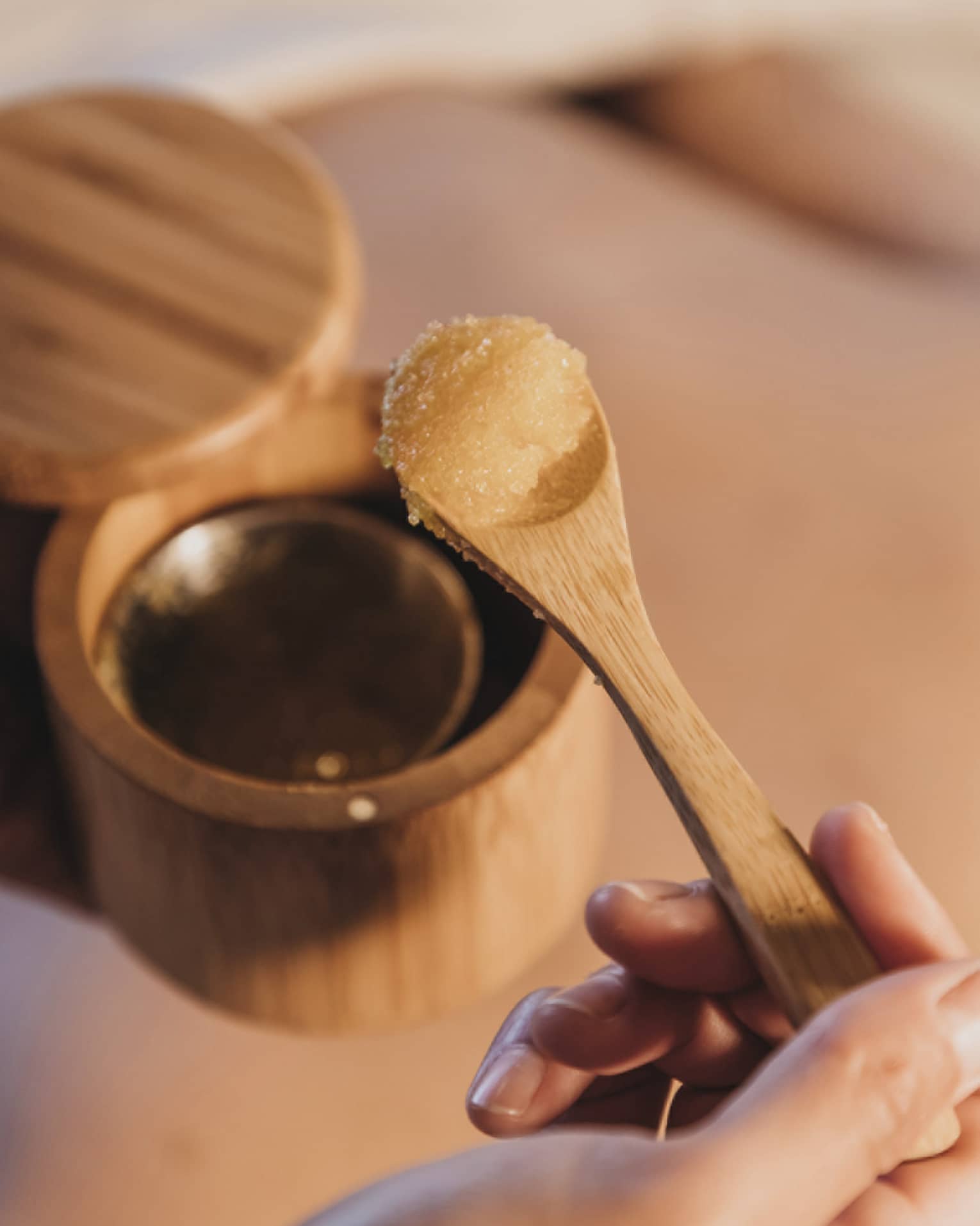 A spa member removing a spa treatment ingredient from a wooden cup with a spoon.