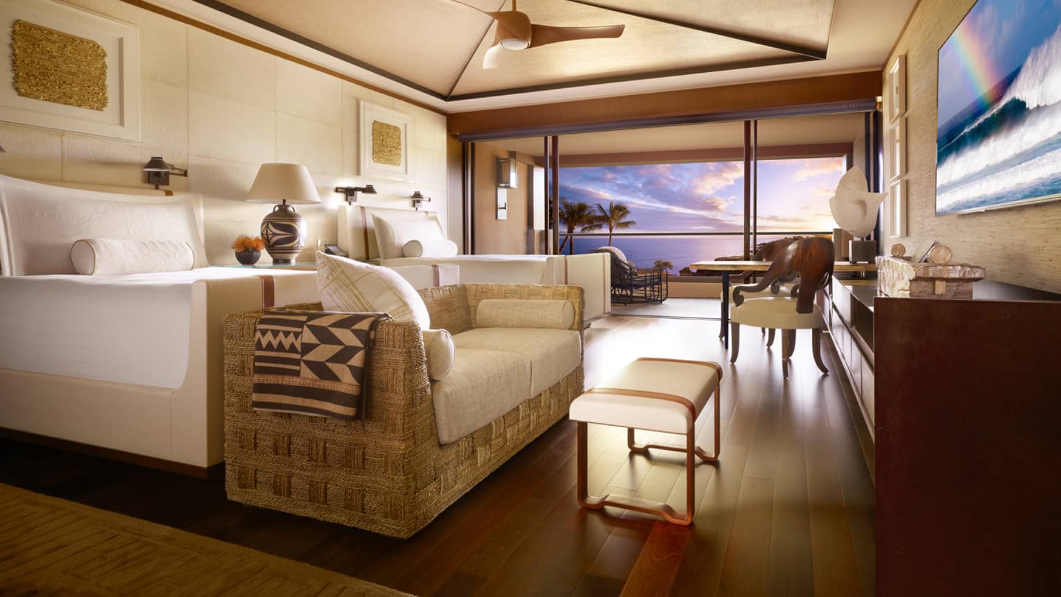 Ocean-View Room bed with loveseat, table at foot by open wall to balcony, sunset