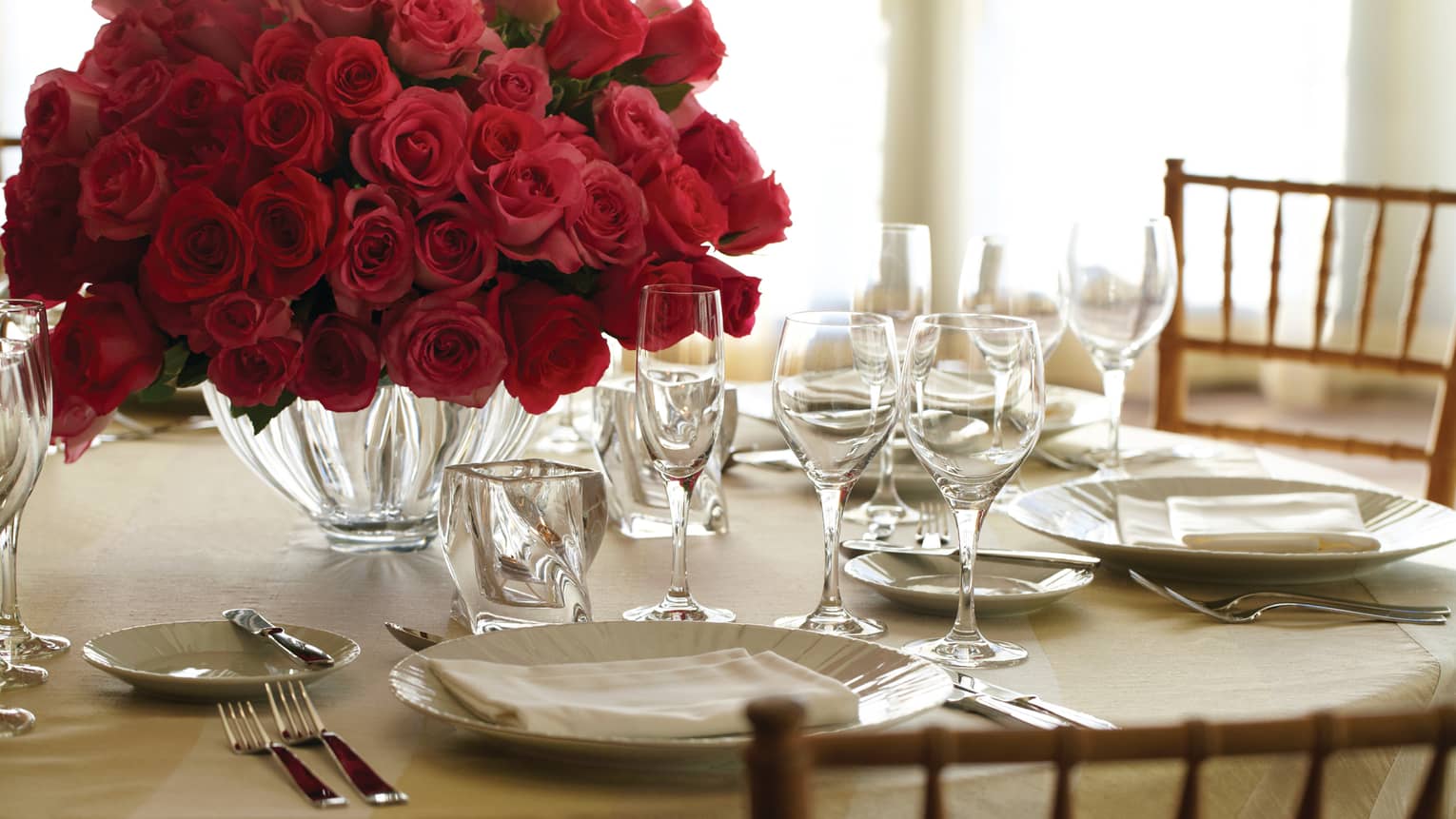 Banquet dining table place setting with plate, crystal glasses and vase with red rose bouquet
