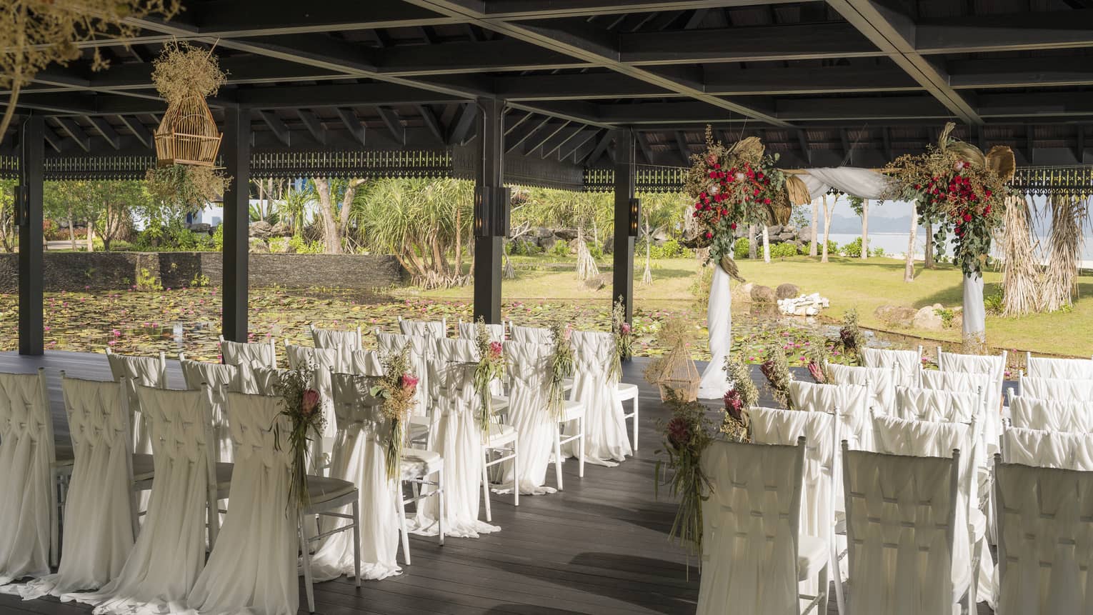 Outdoor wedding reception under pavilion, rows of chairs with white linens 