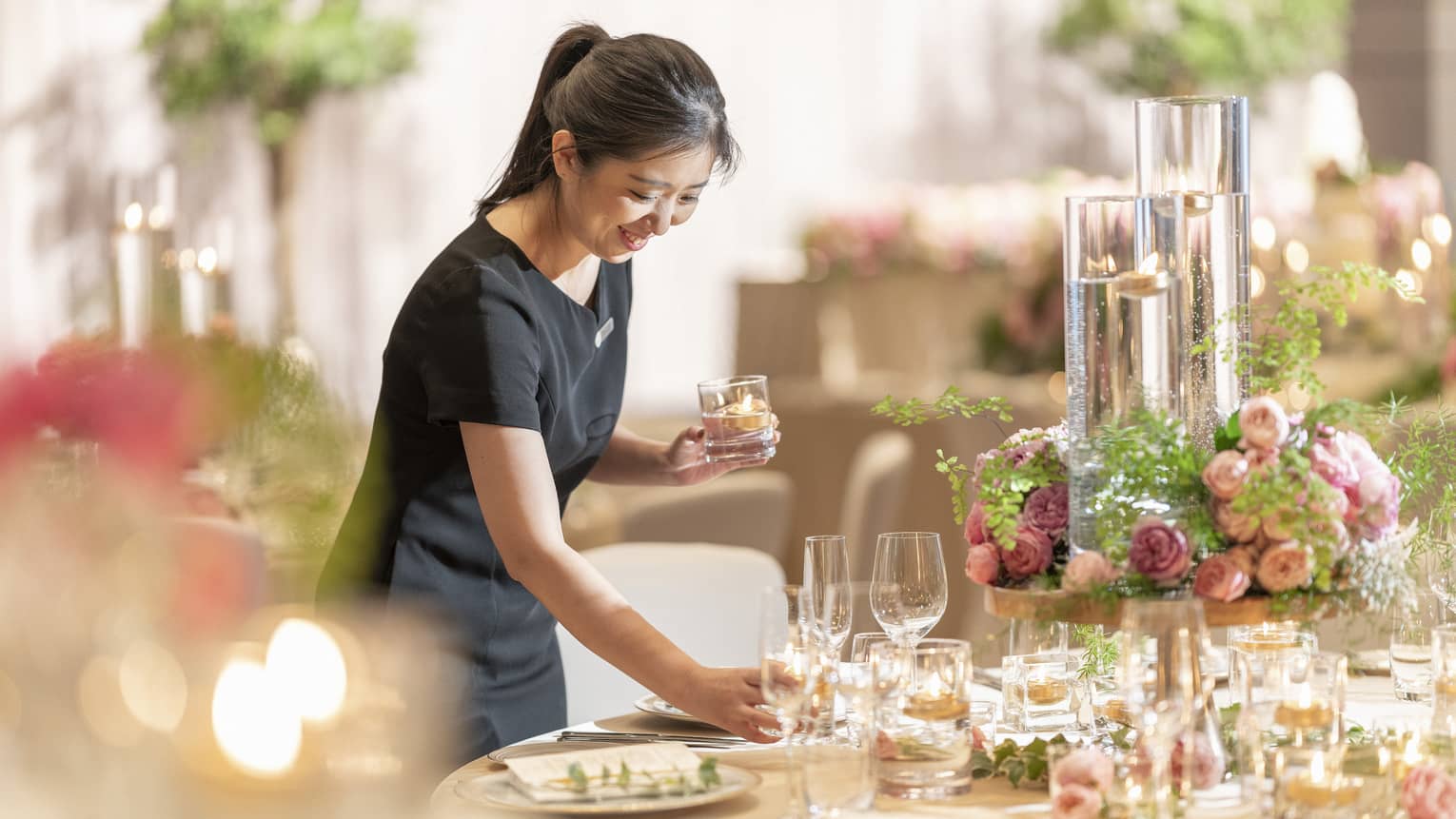 Smiling FS staff member sets table in ballroom with pink flower centrepiece