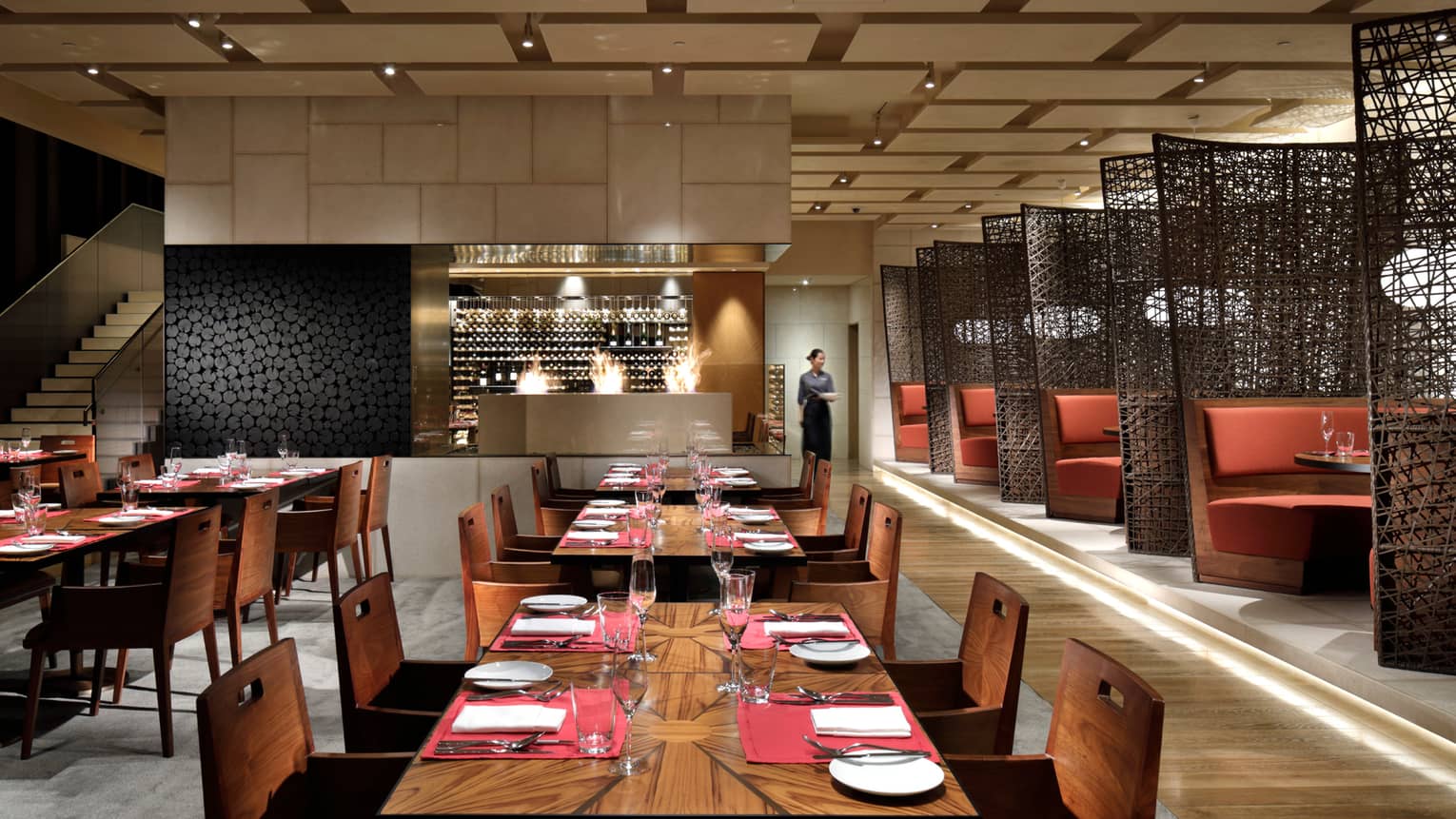 Modern dining room with rows of wood tables, large wine cellar, booths by black woven screens
