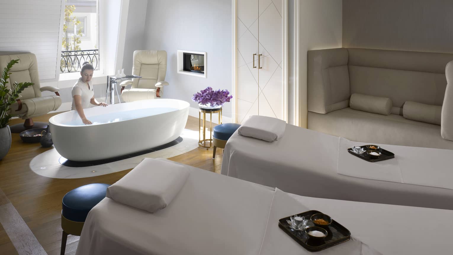 Two white spa beds side-by-side with yellow sashes, trays with salts and oils, woman makes bath