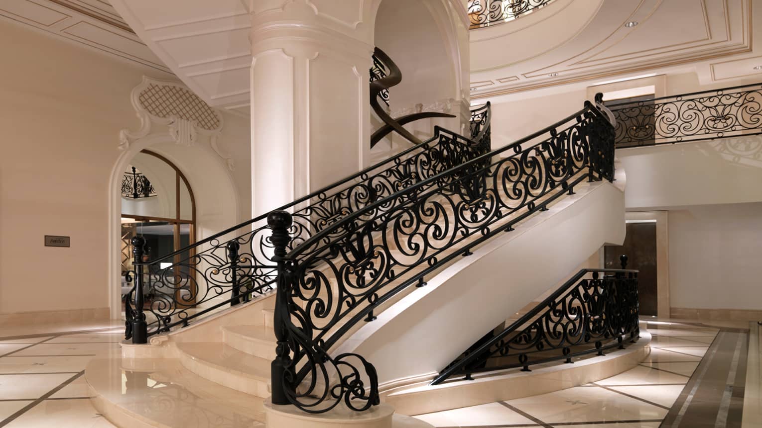 Hotel Beaux-Arts style white staircase with decorative black railings, white pillar, white tile floor