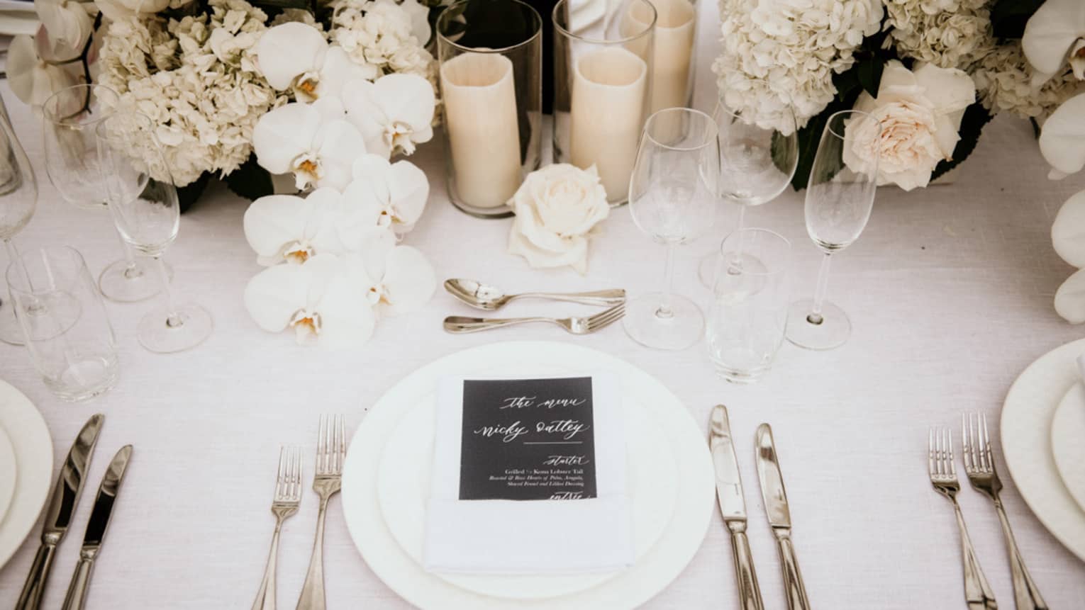 Wedding table setting with white flowers and candles, menu on white napkin and plates