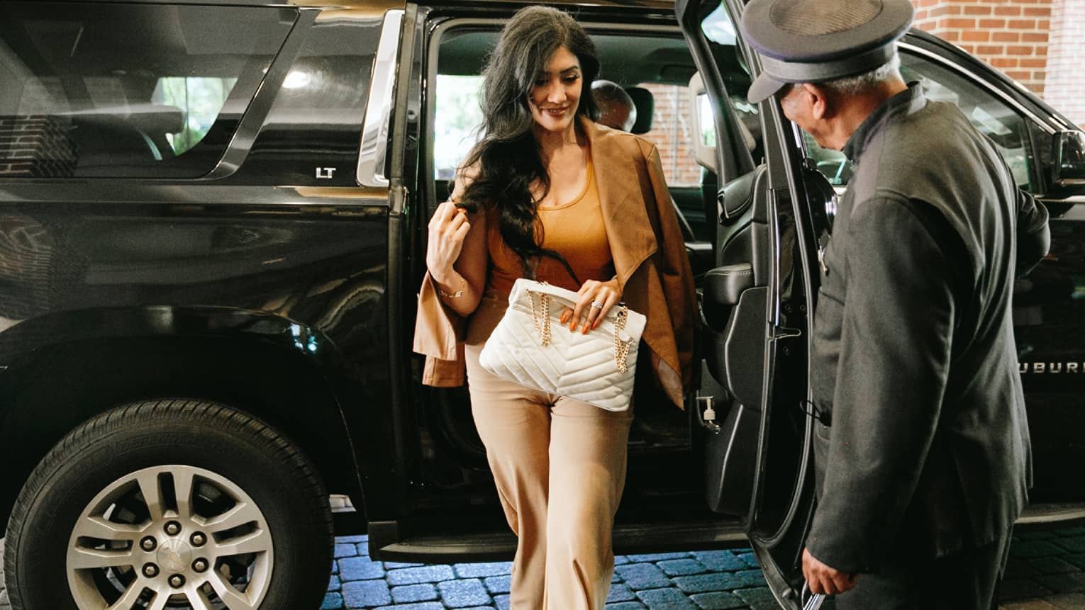 A woman getting out of a suv while a member of staff holds the door.