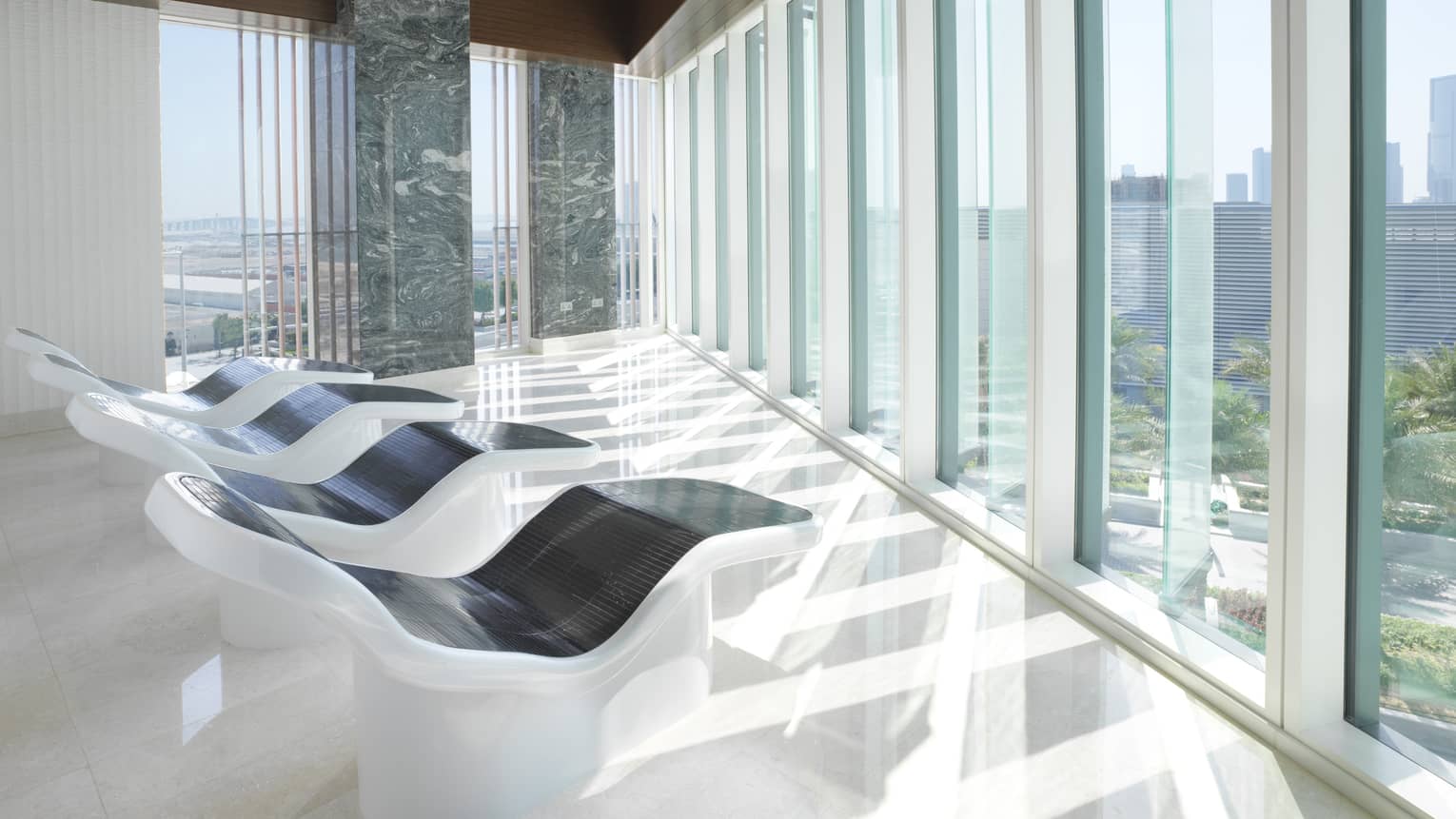 White-and-black recliners in front of floor-to-ceiling glass windows in bright relaxation room