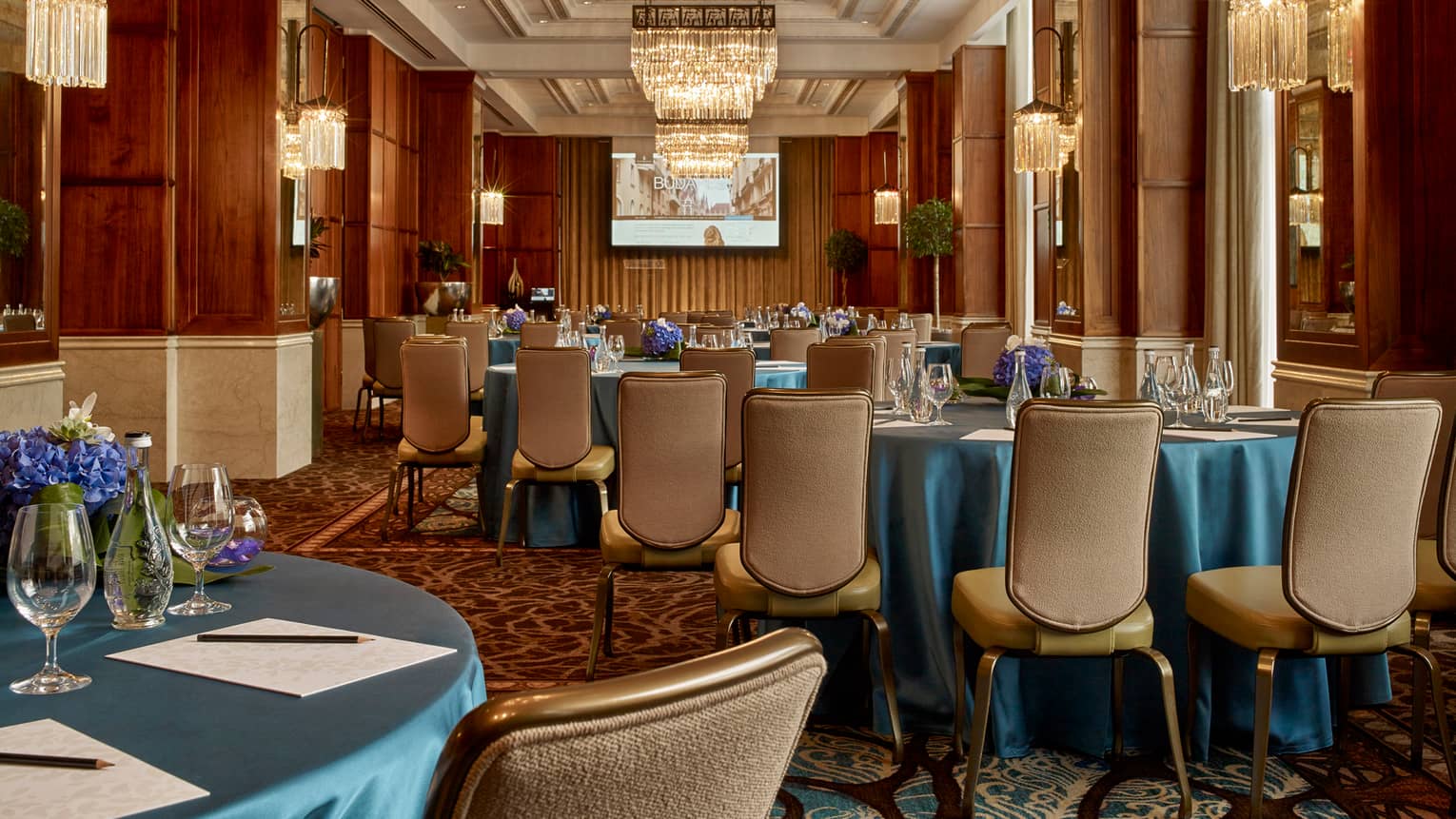 Gresham Room Art Nouveau-style ballroom tables with blue satin tablecloths, leather dining chairs, chandeliers