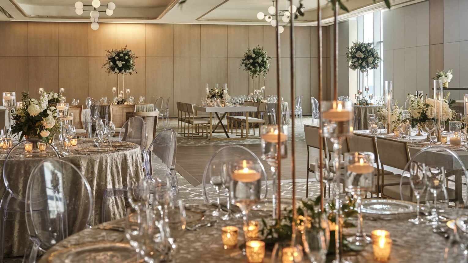 A large room with round tables, flower centerpieces and candles.