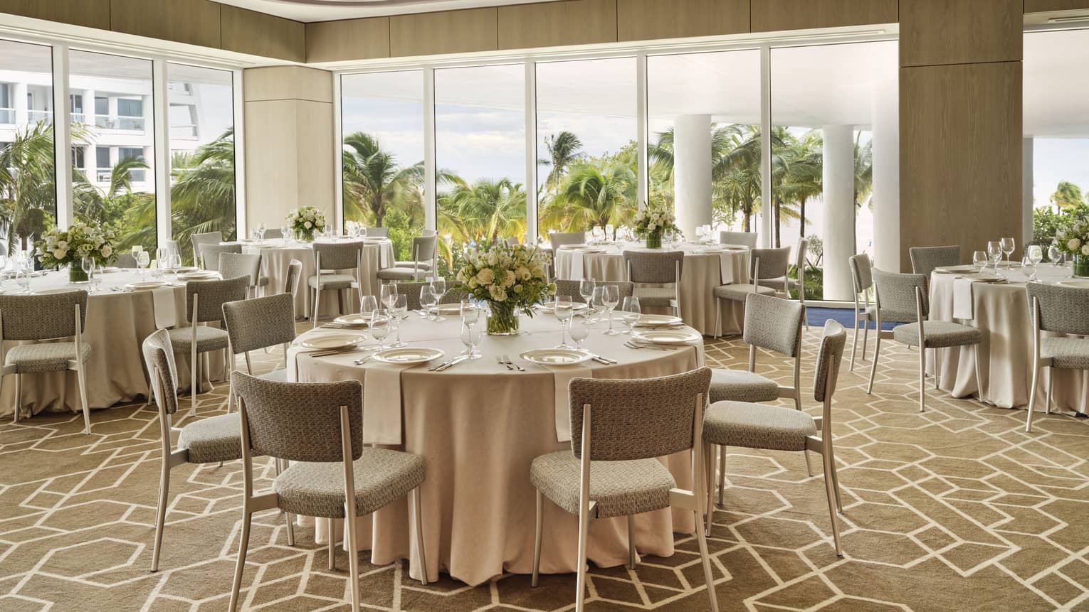 A large meeting room with round tables, large windows and blue chairs.