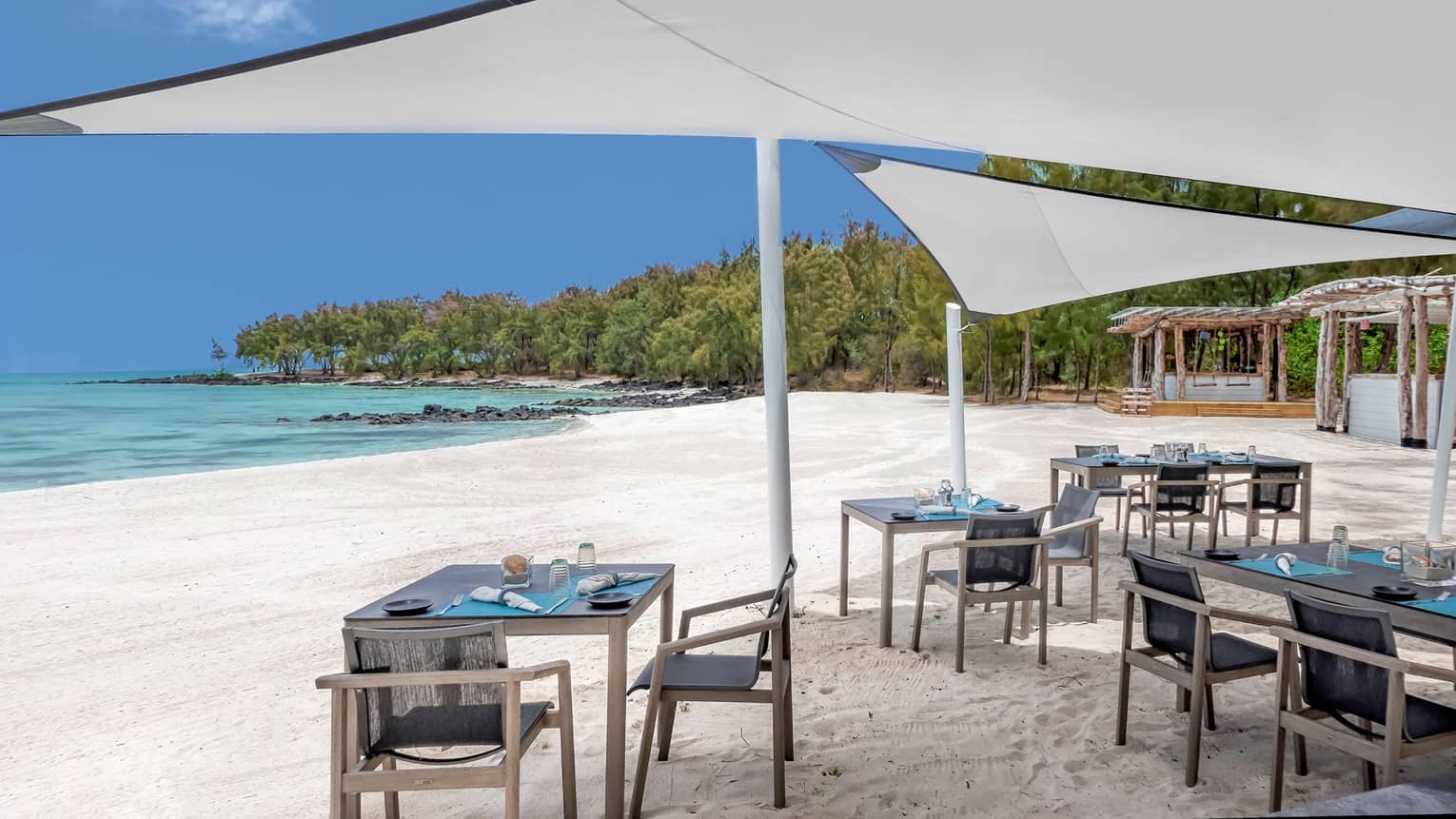 Small dining tables under white umbrella canopies on white sand beach near ocean