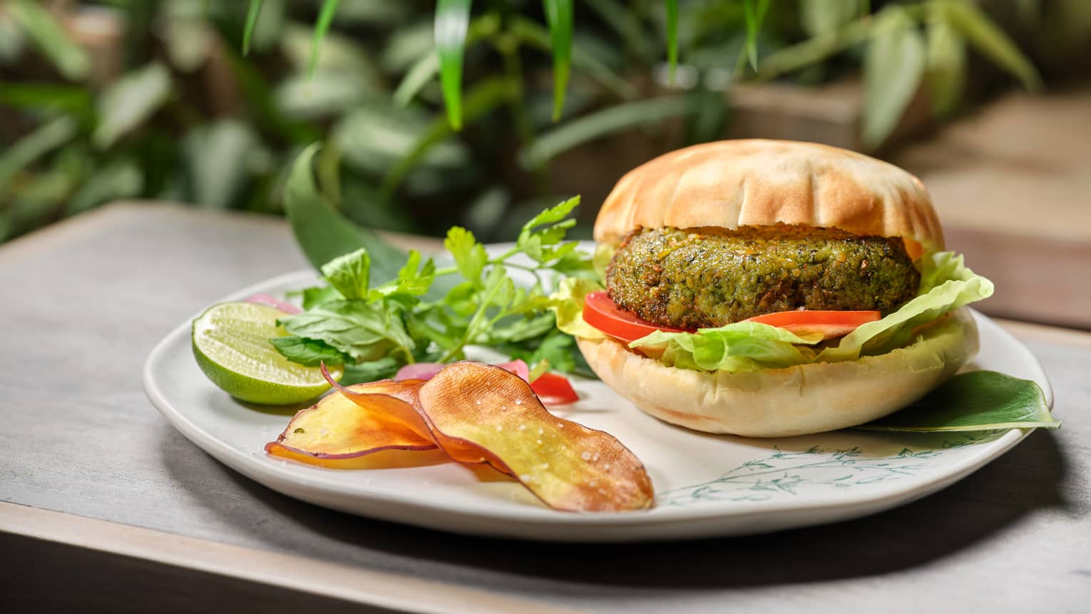 Green-hued vegetable burger with fresh herbs and lime cheek on round white plate