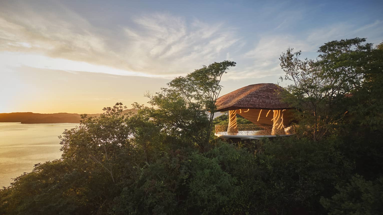 Exterior view of a covered wellness shala set on a hillside overlooking the ocean