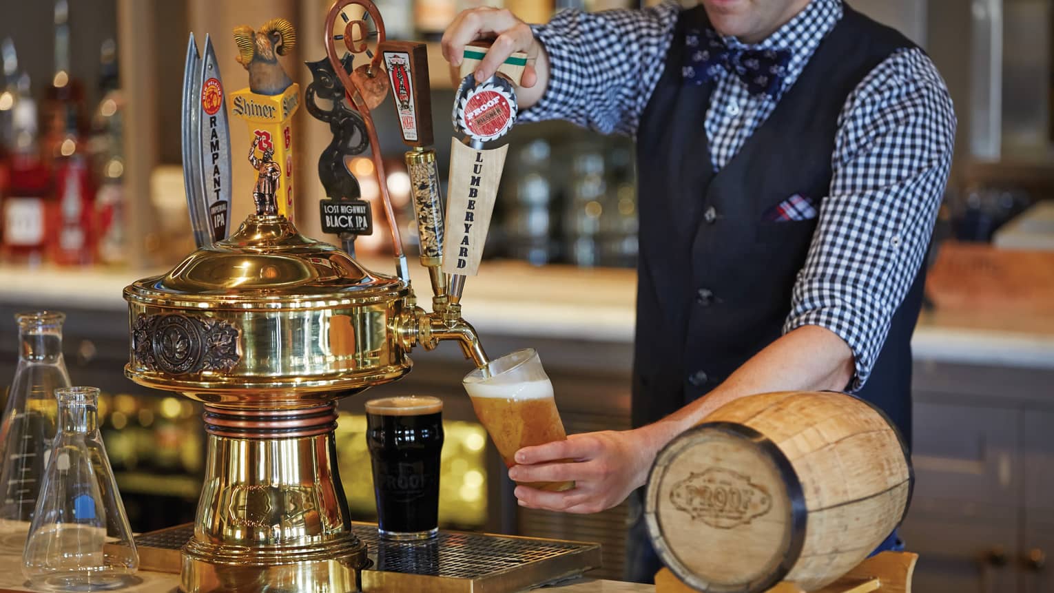Bartender in vest, uniform pours beer into pint glass from taps at bar 