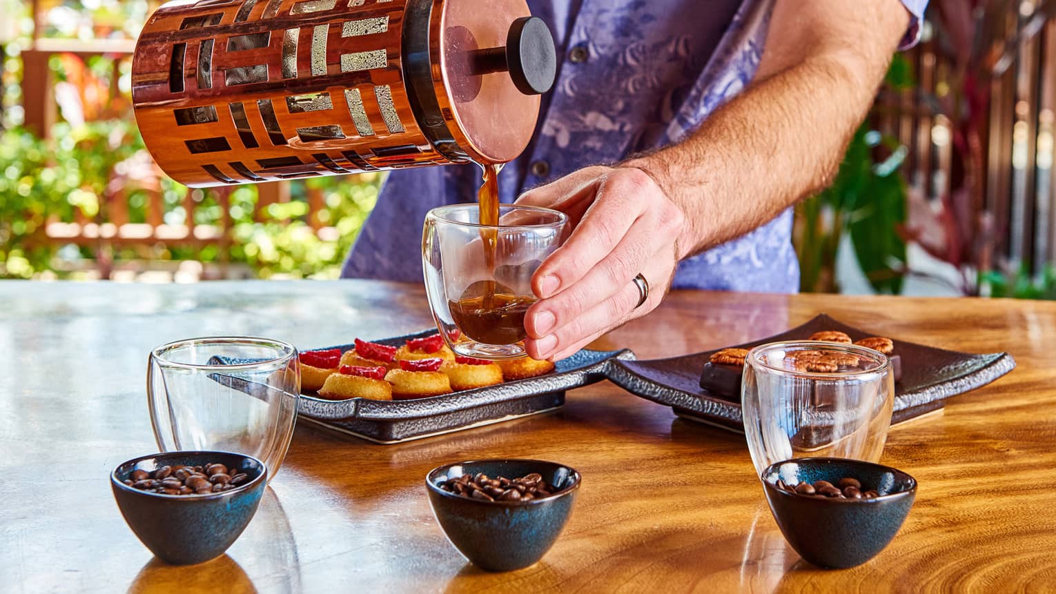 Server pouring coffee from carafe into tasting mugs, desserts on trays, bowls with beans