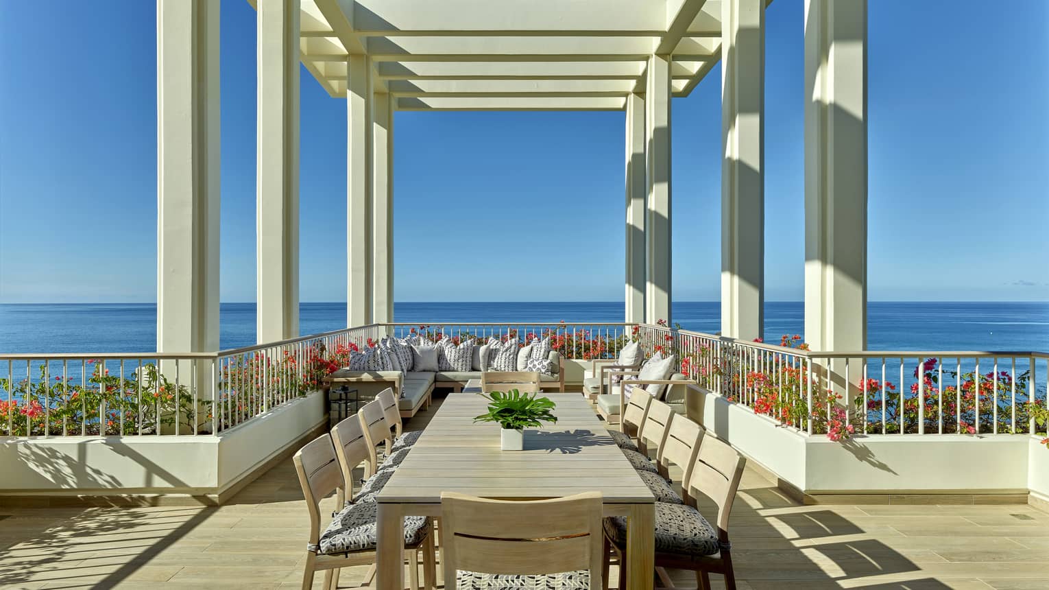 Ocean-view terrace with long dining table under pergola