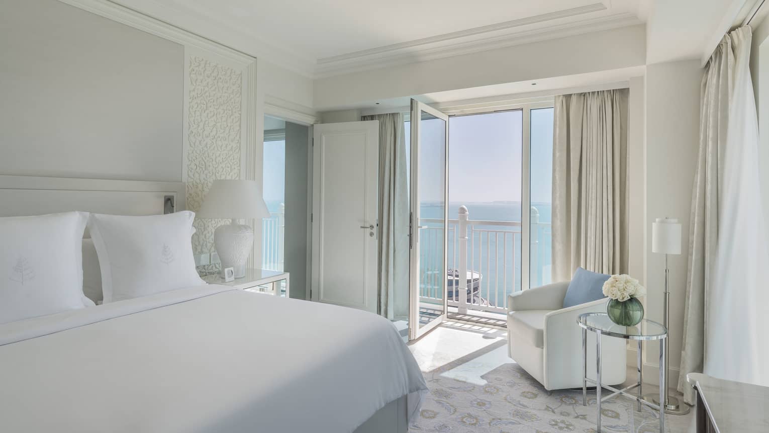 A suite with a large white bed, and an open balcony overlooking the sea.