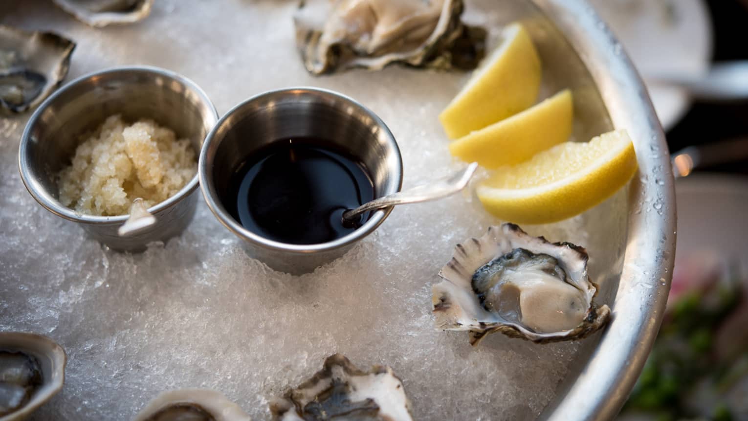 Half-shell oysters, lemon wedges on ice in silver platter