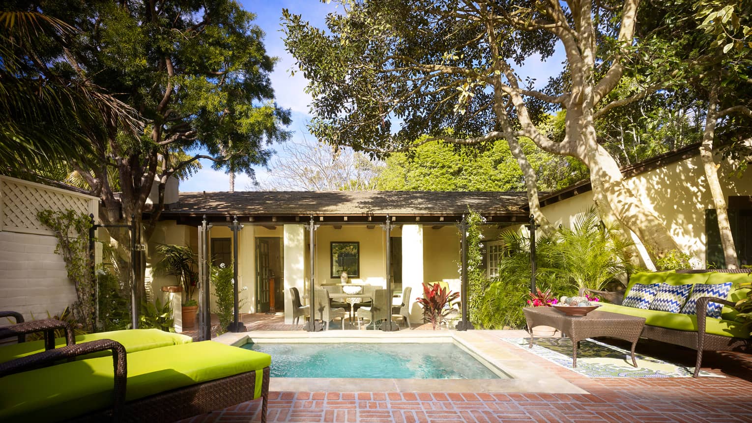 Bungalow backyard with plunge swimming pool, patio, wicker lounge chairs with green cushions