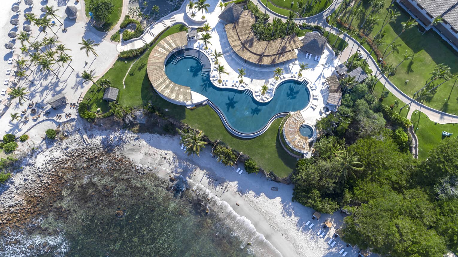 An overhead view of a hotel with a large pool near a beach shore.