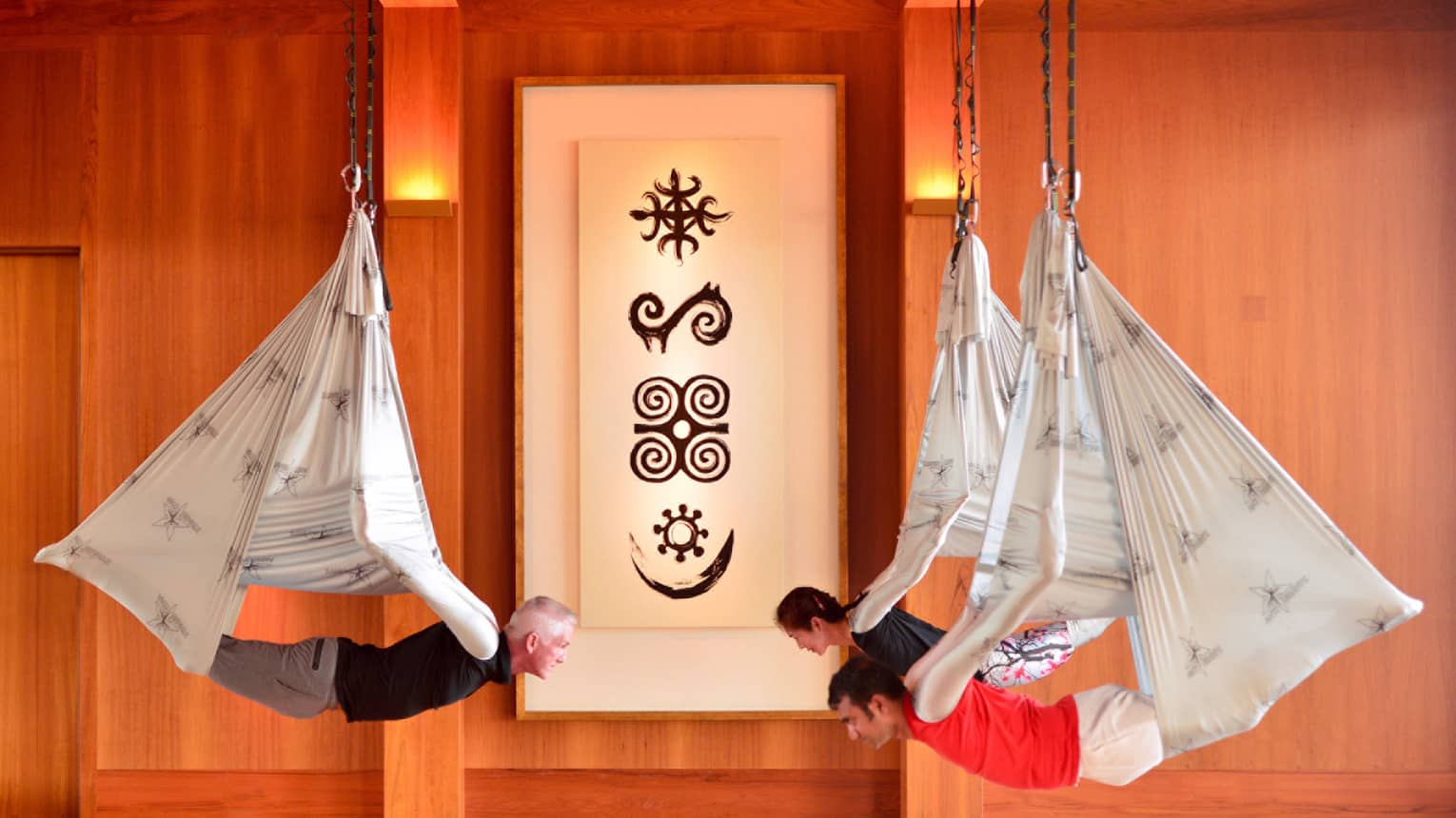 Men, woman hang from silk hammocks during anti-gravity yoga session