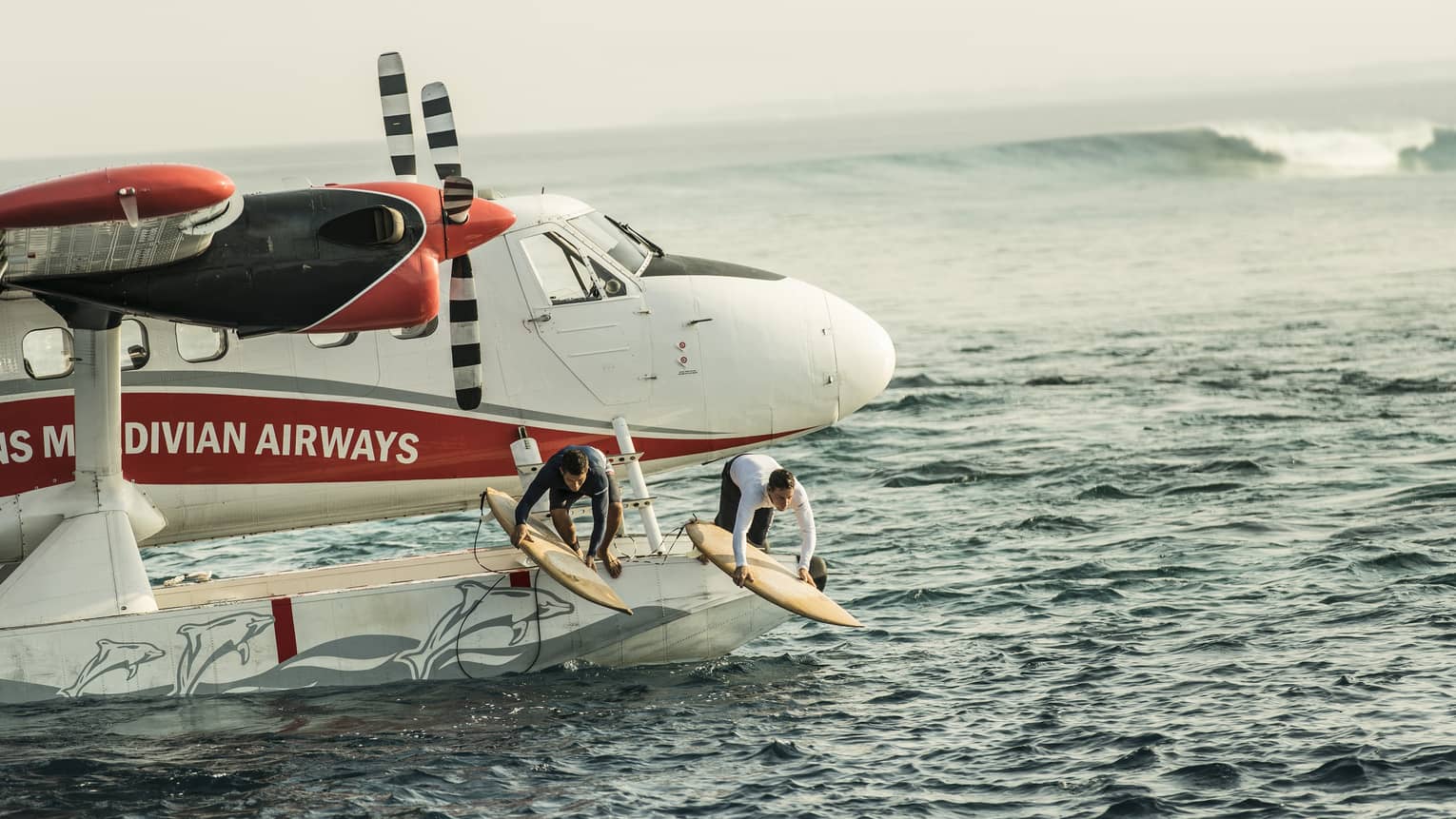 Two people with surfboards jump from float plane onto waves