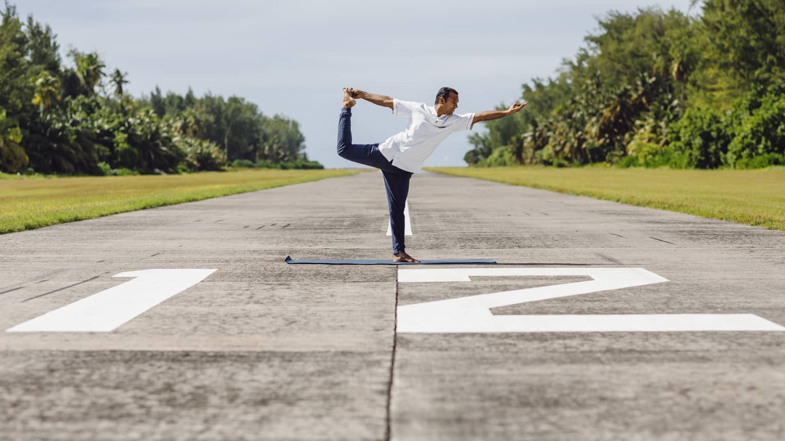 A man doing yoga – specifically ballerina pose – on an airplane runway