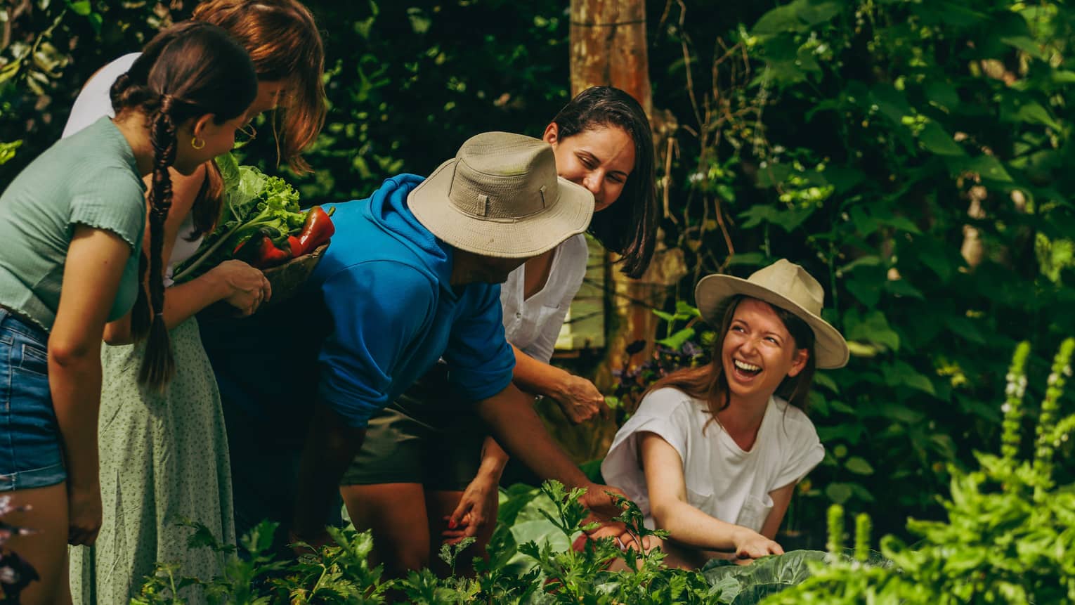 A group of people in an herb garden laughing while holding vegetables.