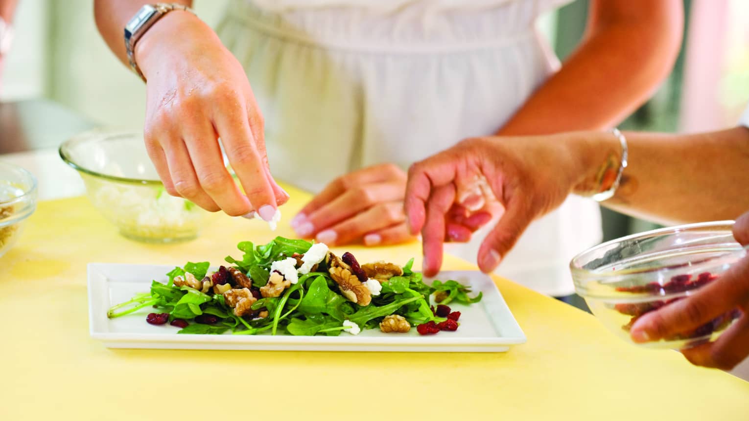 Two people making a salad on a white plate.