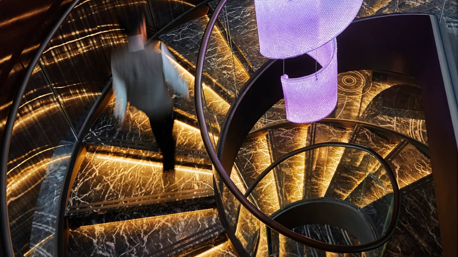 Server in uniform walks up black marble spiral staircase with orange lights 