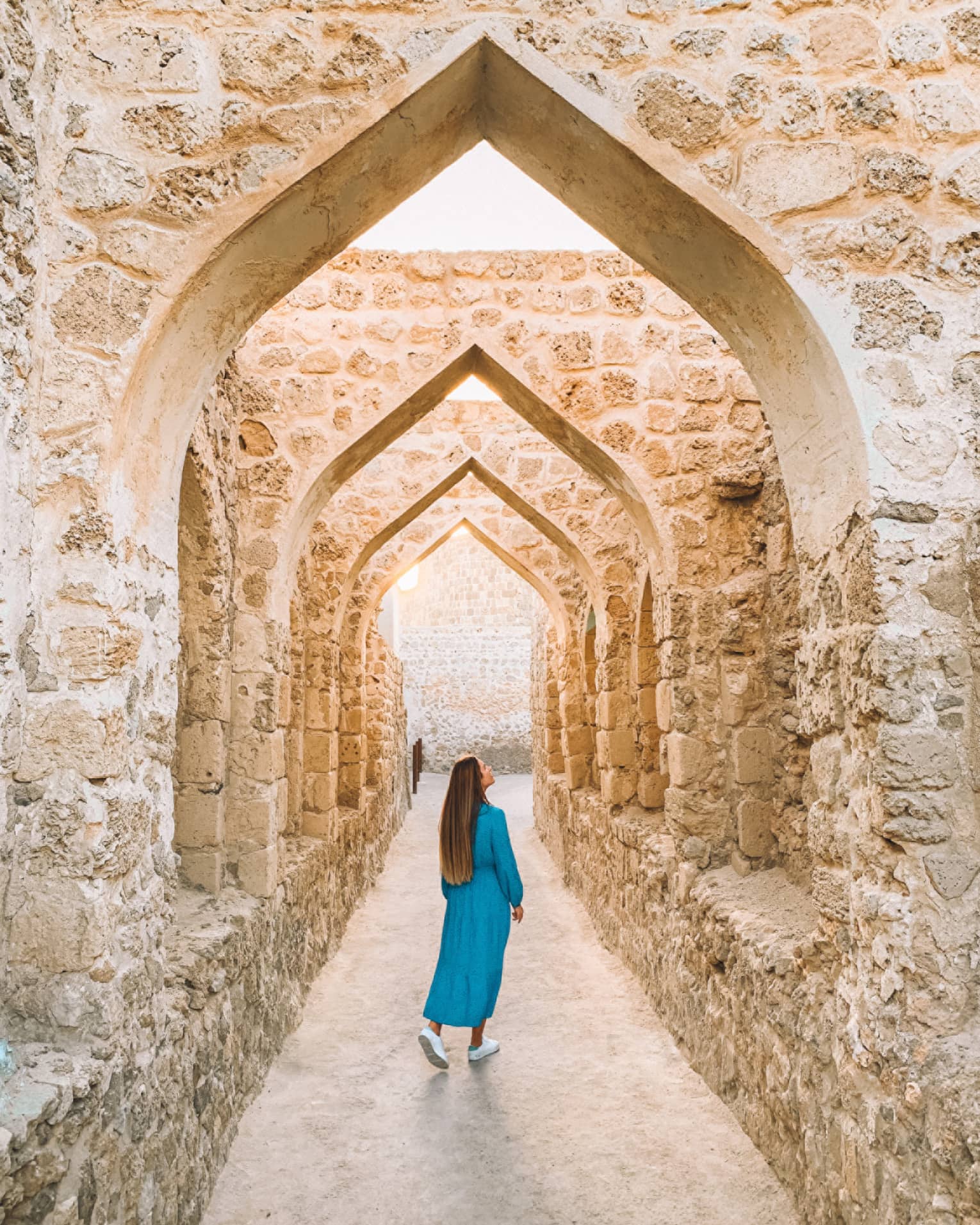 A woman stands underneath a stone pathway.